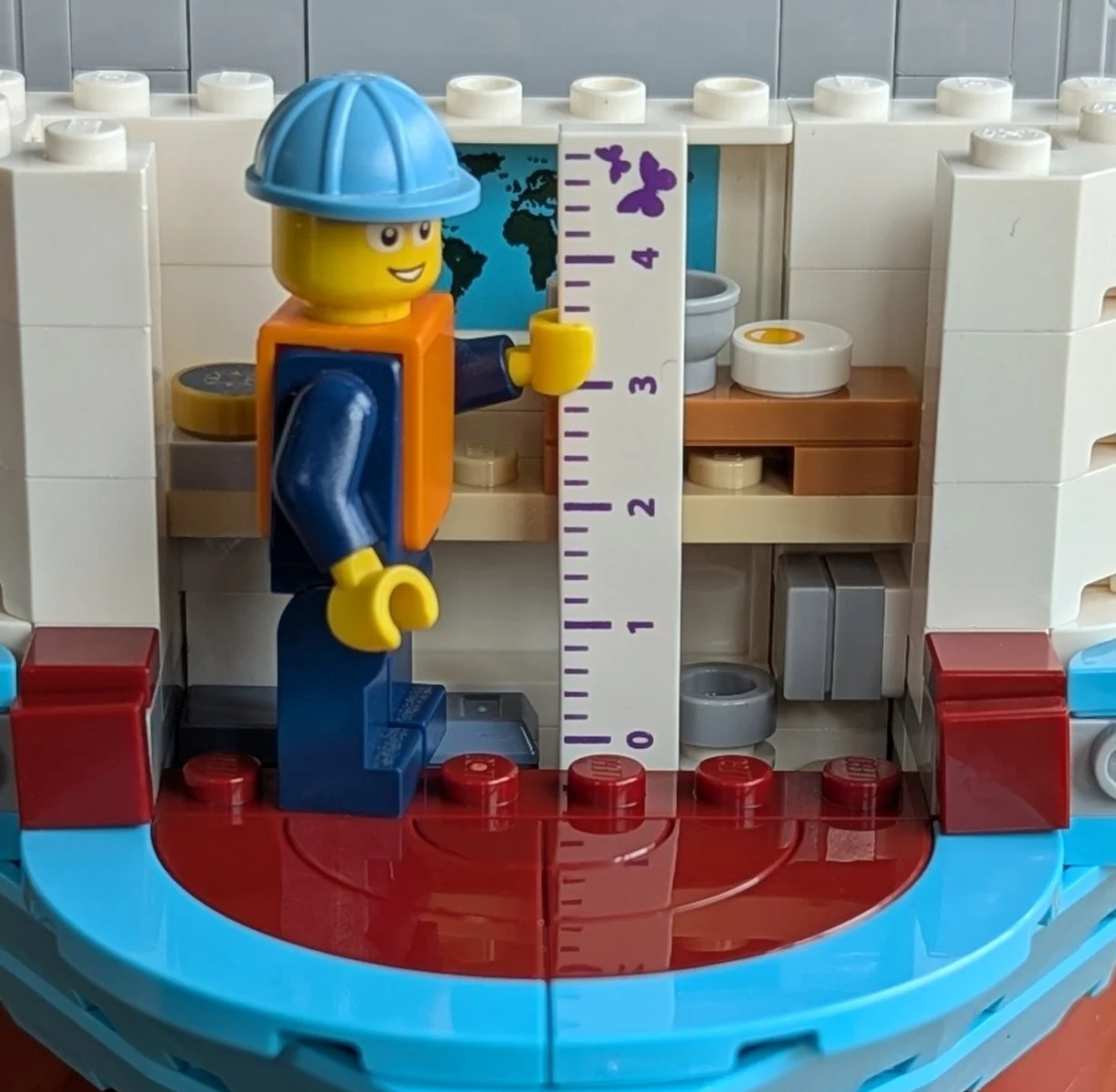 Construction worker minifig with a Friends ruler in front of the accomodation block interior.