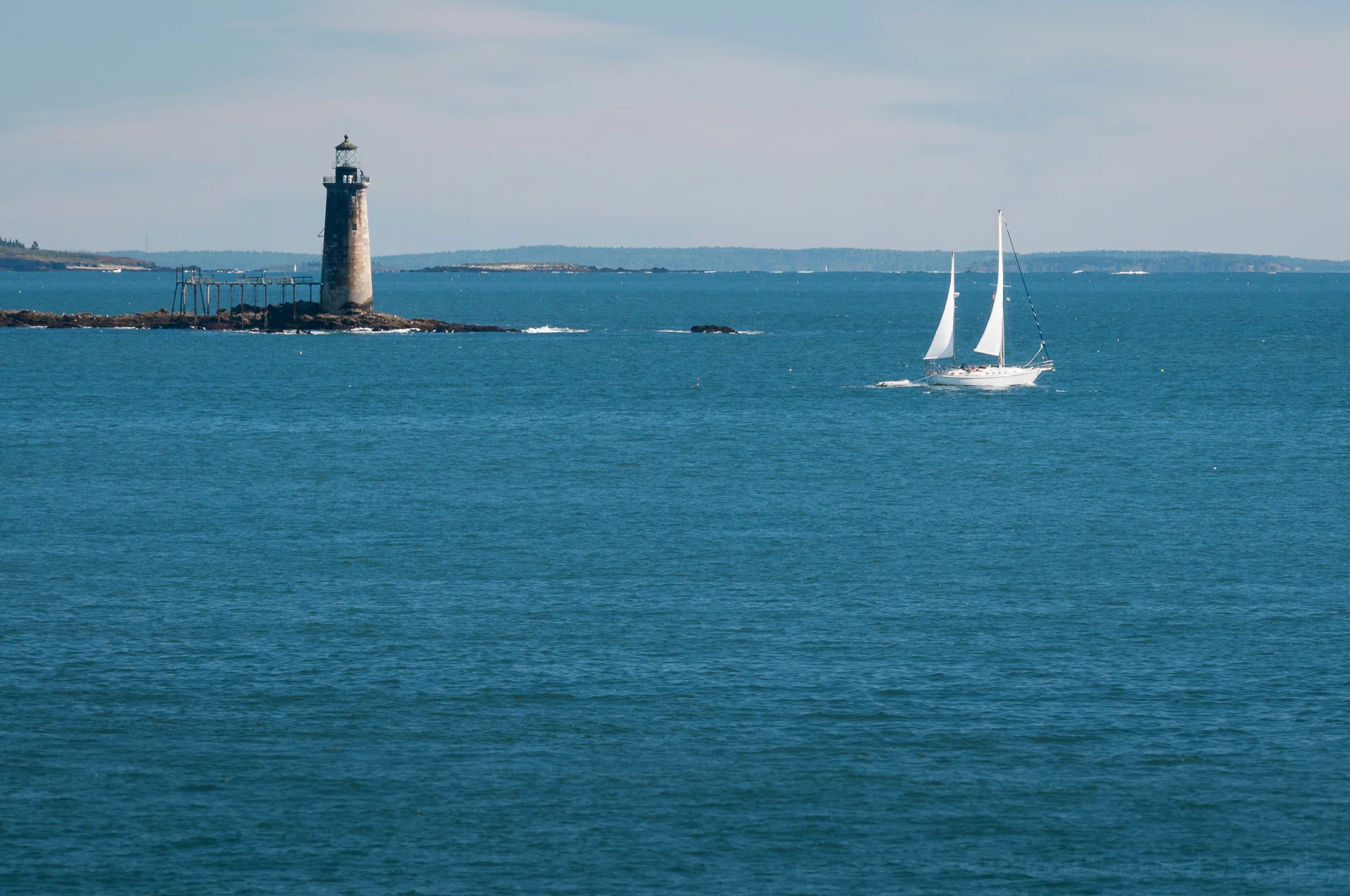 Ram Island Ledge Light, in Maine, with white sailboat in foreground