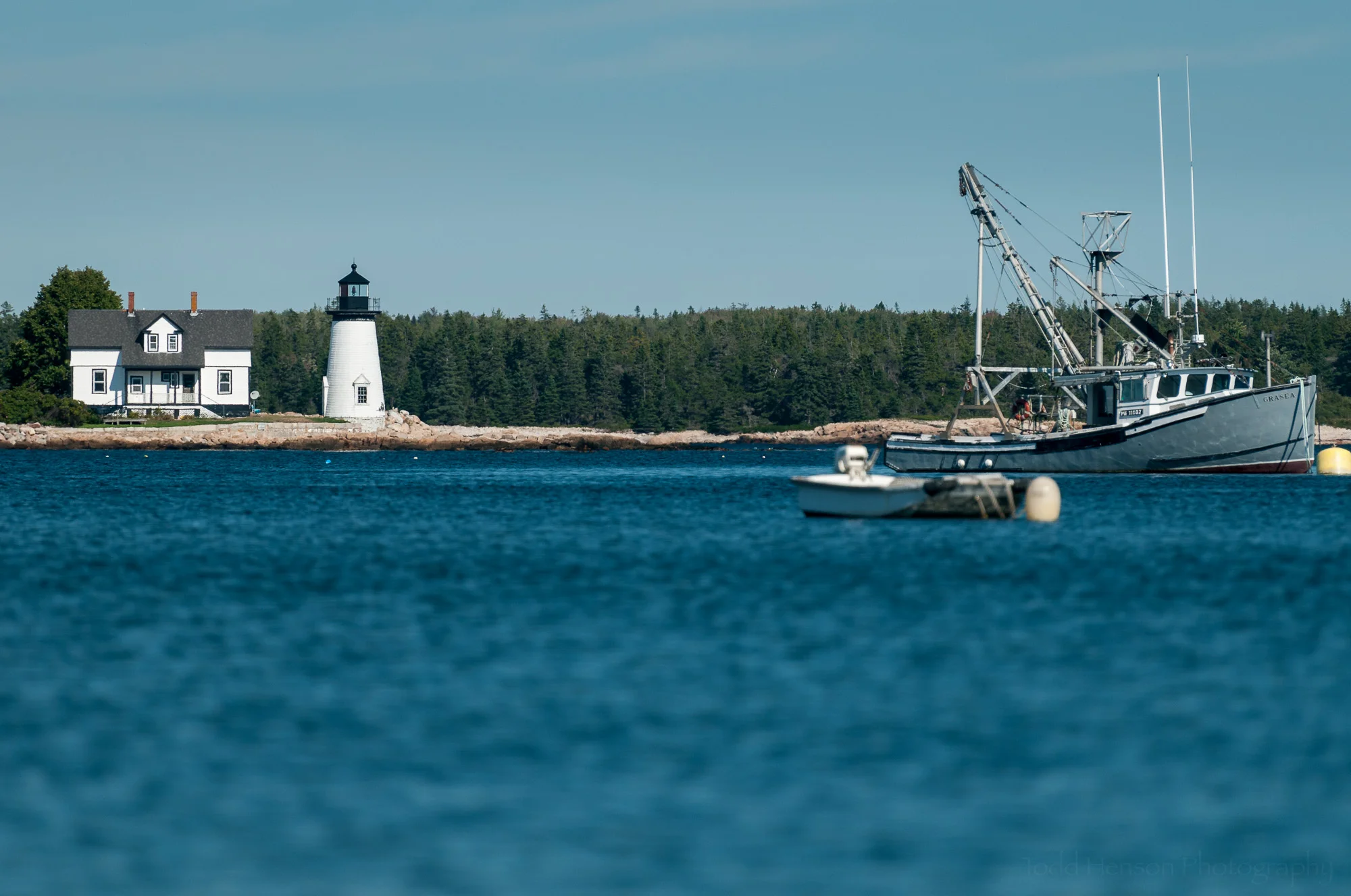 Prospect Harbor Light, Maine, with fishing boats in Inner Harbor, viewed from the shore of Prospect Harbor