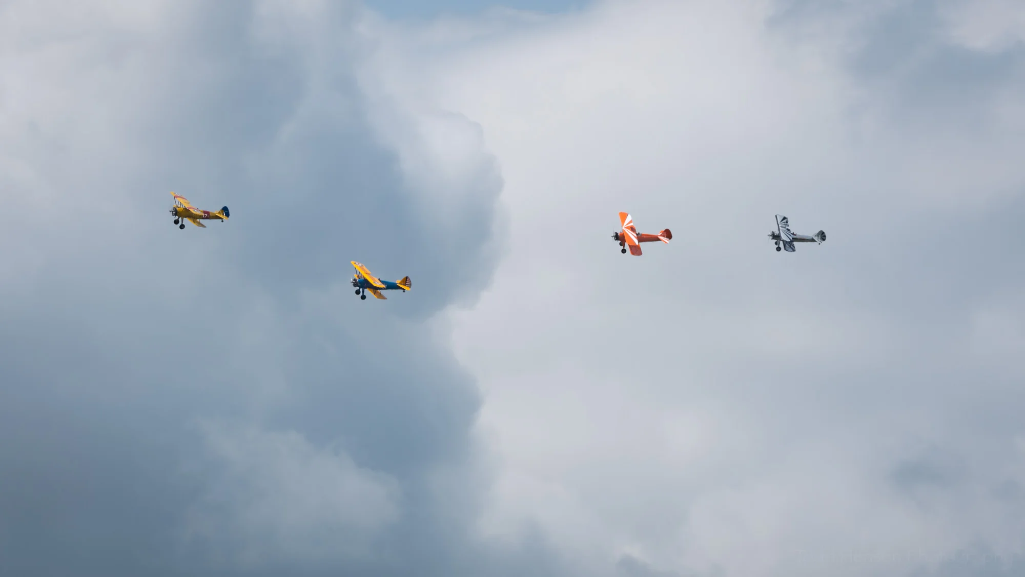 Four biplanes from the Bealeton Flying Circus flying in formation against the cloudy sky.