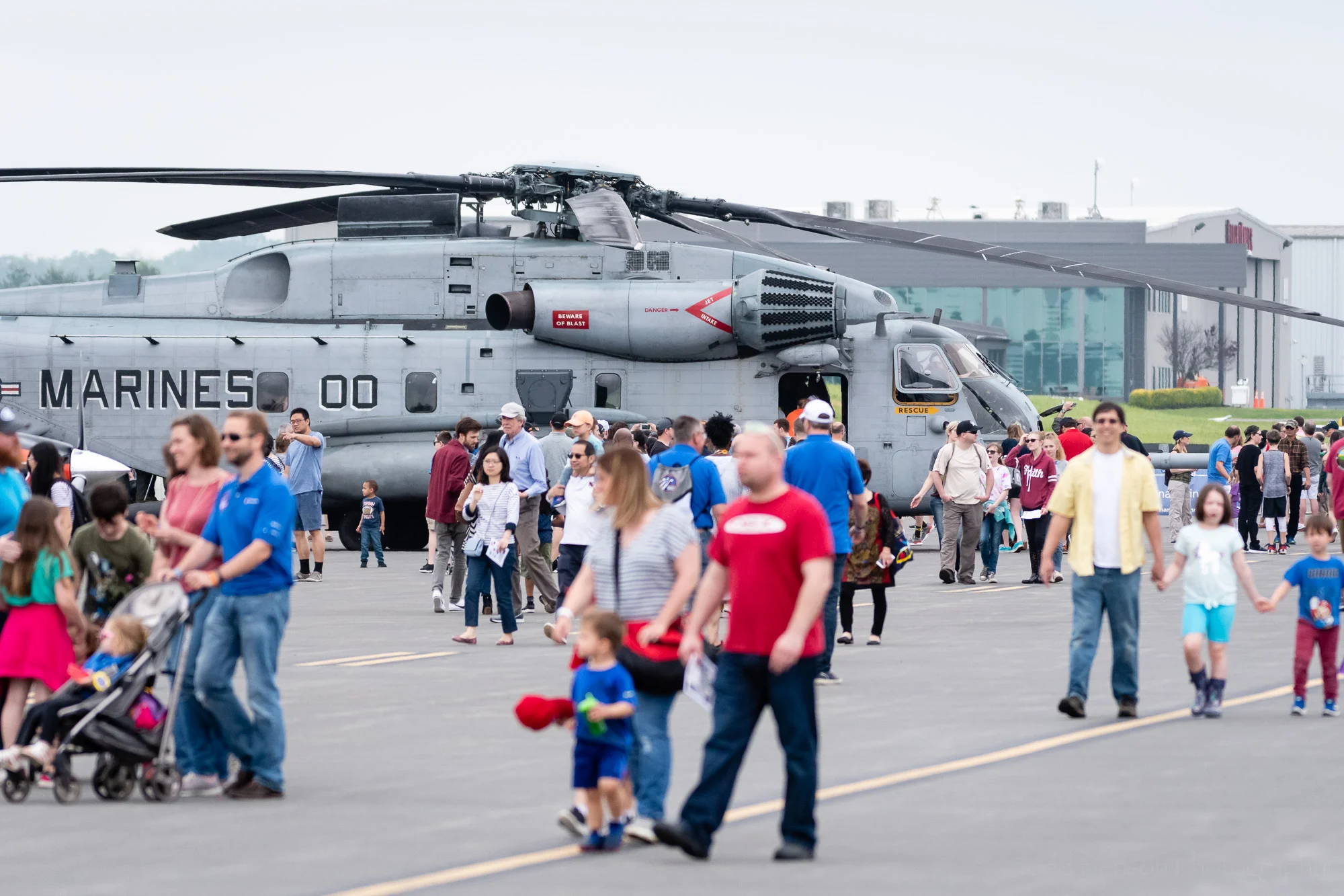 Crowds walking around the 2019 Manassas Airshow, with a US Marine Super Stallion CH-53 helicopter in the background.