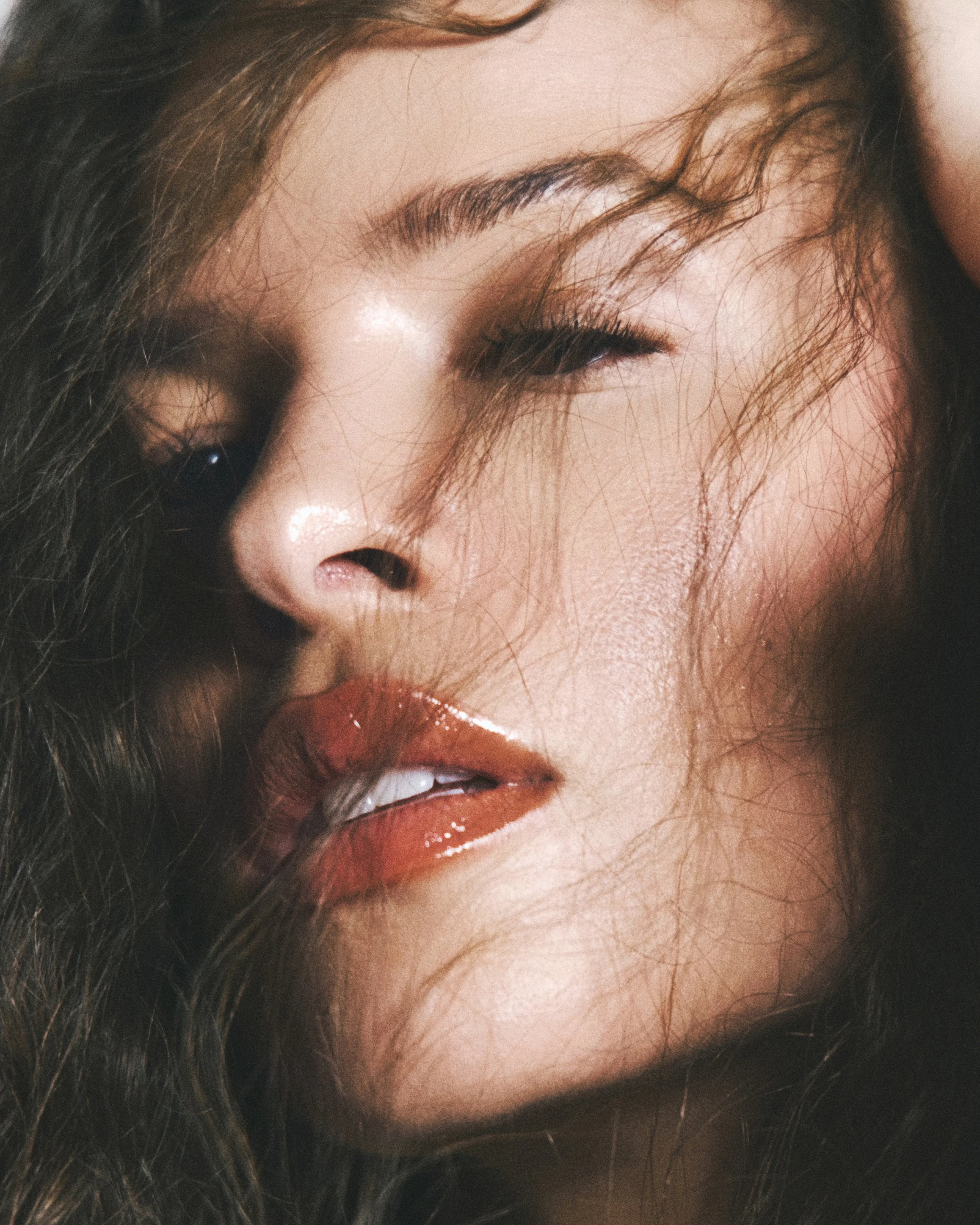 Close-up of a woman's face with makeup, showing her eye, eyebrow, and lips, with brown hair partially covering her face.