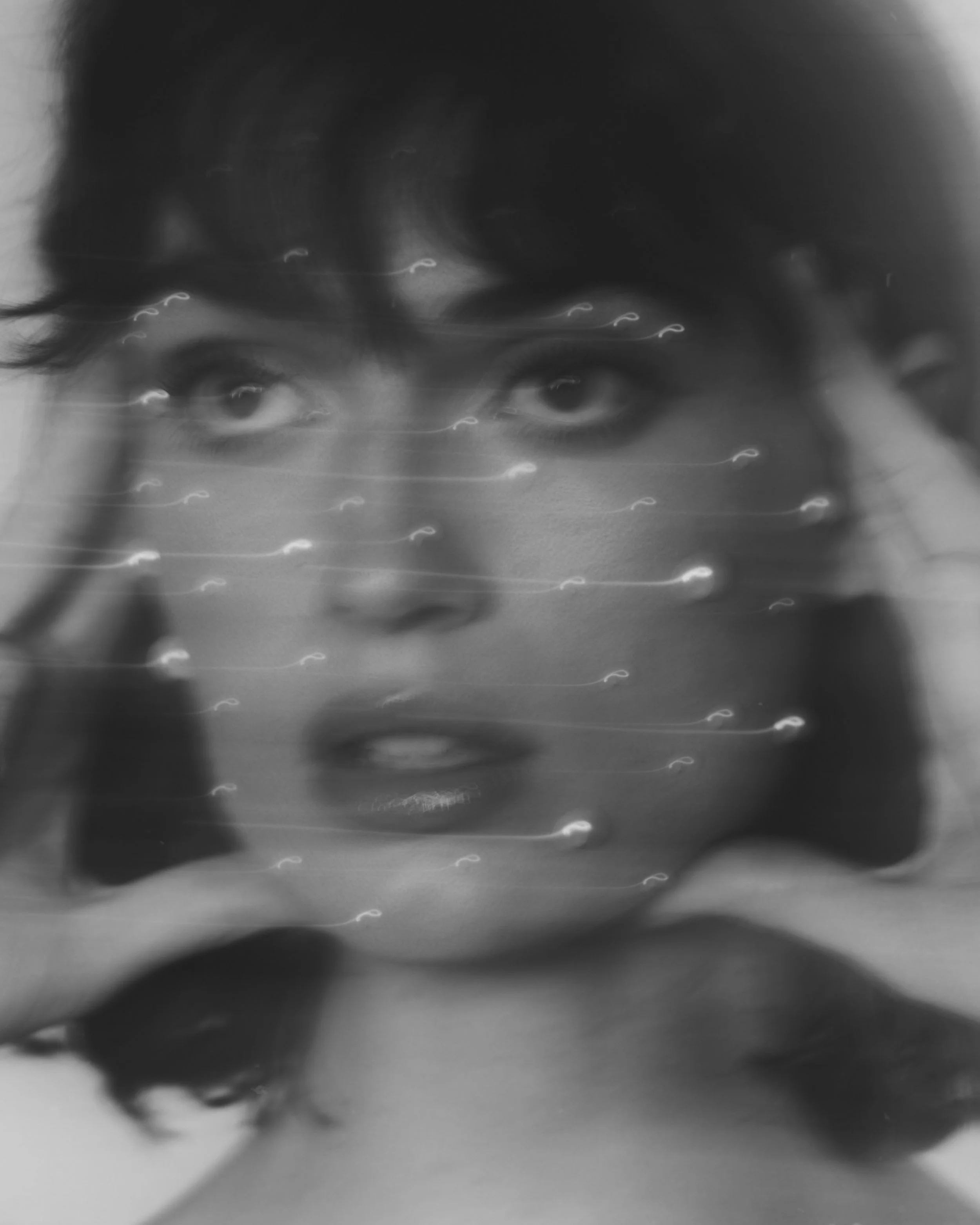 Black and white photo of a person's face with their eyes looking directly at the camera, with a digital overlay of small white icons or symbols, creating a layered visual effect.