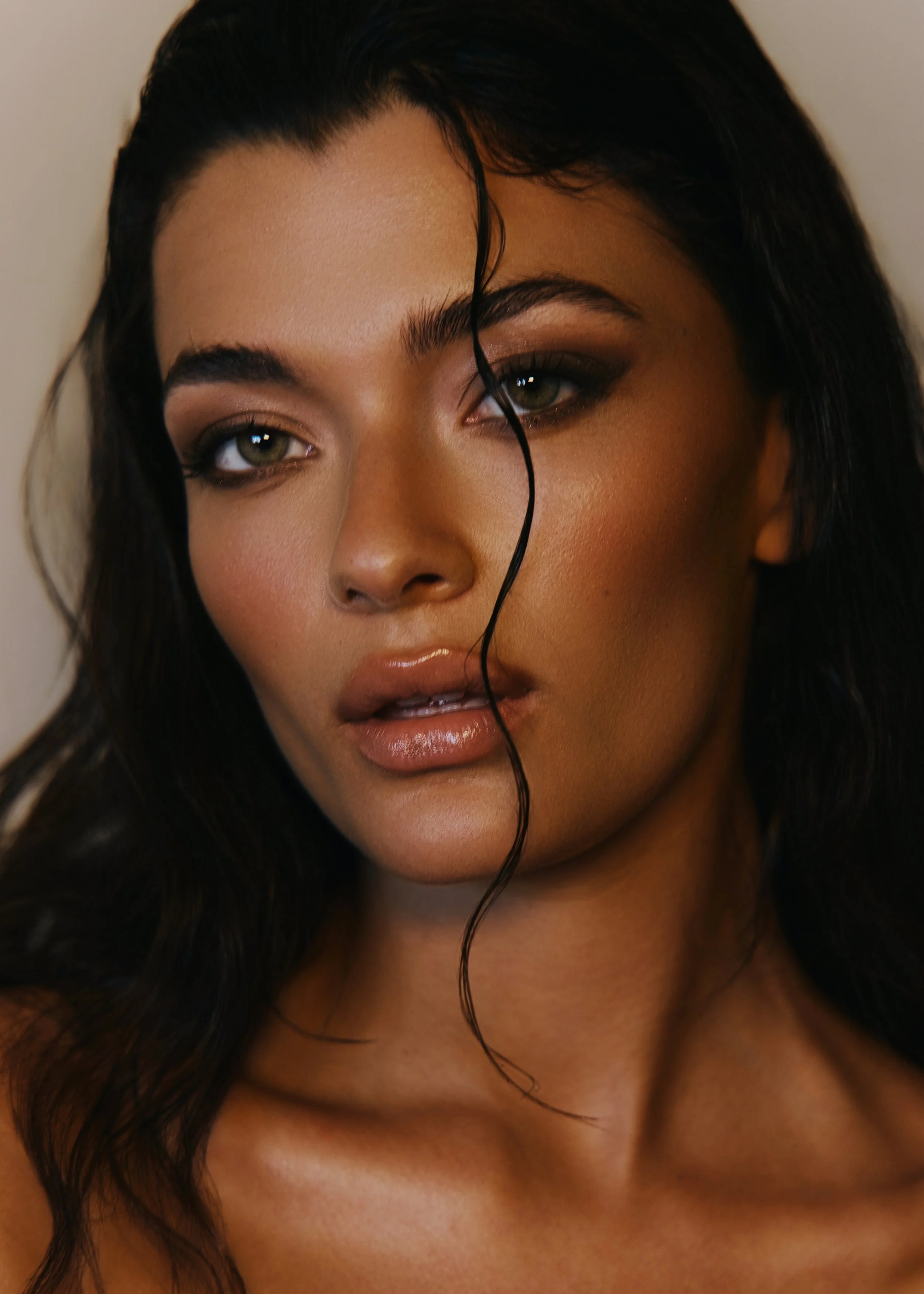 Close-up portrait of a woman with dark, wavy hair and makeup, looking slightly to the side with a neutral expression.