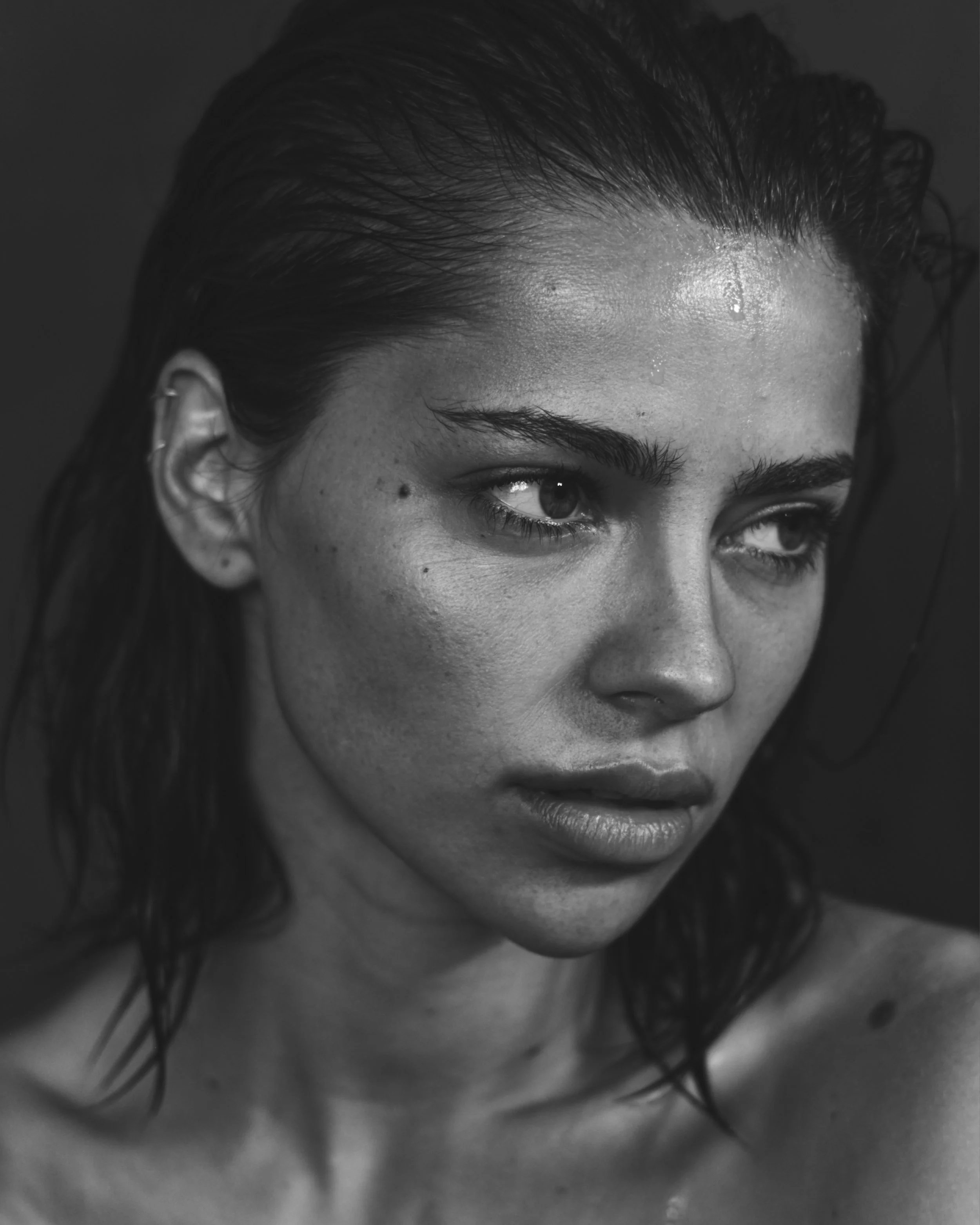 A close-up black and white photo of a woman's forehead, eyebrows, upper eyes, and some wet hair strands with moisturized skin.