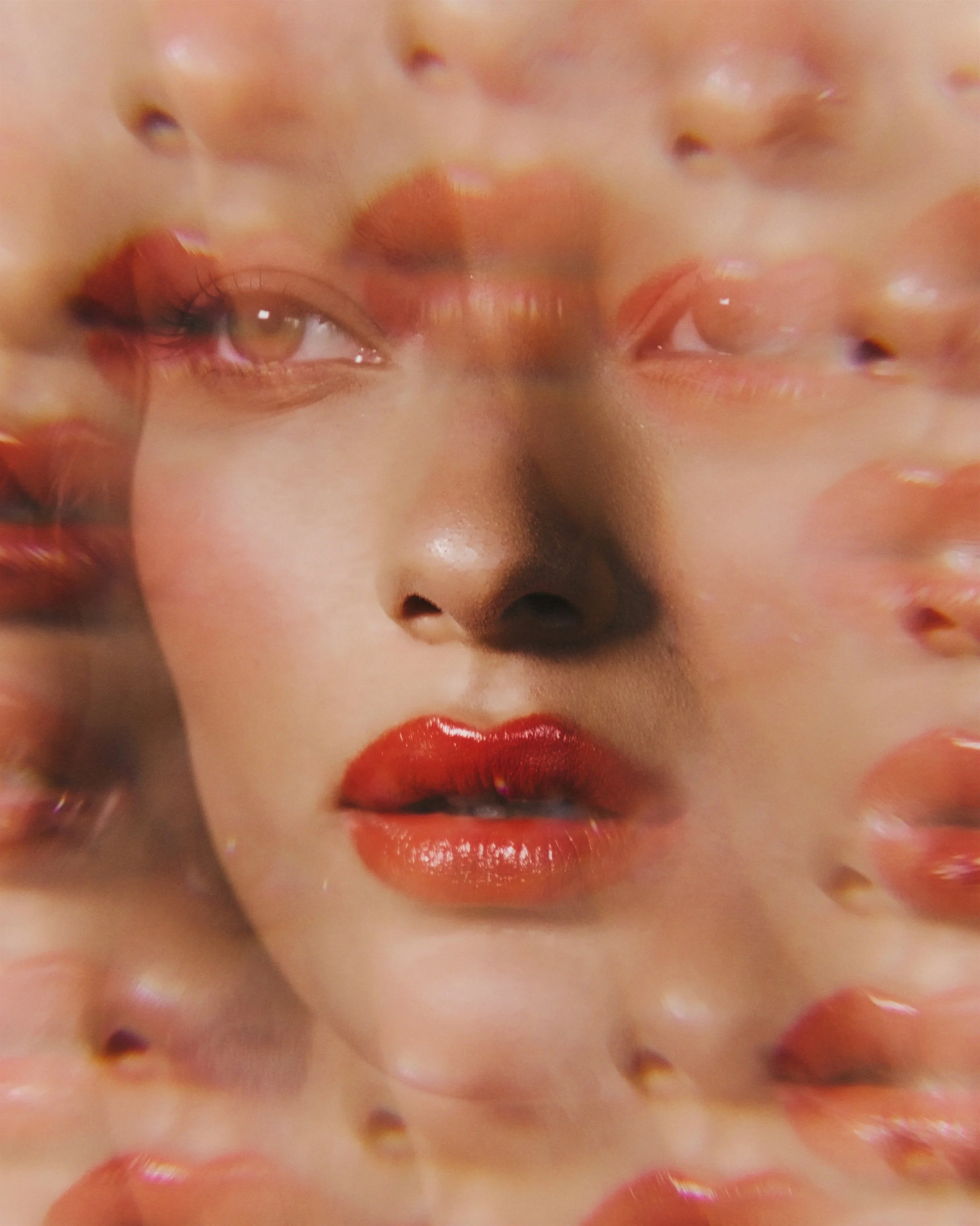 A highly blurred and distorted close-up of a person's face, focusing on the lips, nose, and eye area, with vibrant makeup and skin tones.