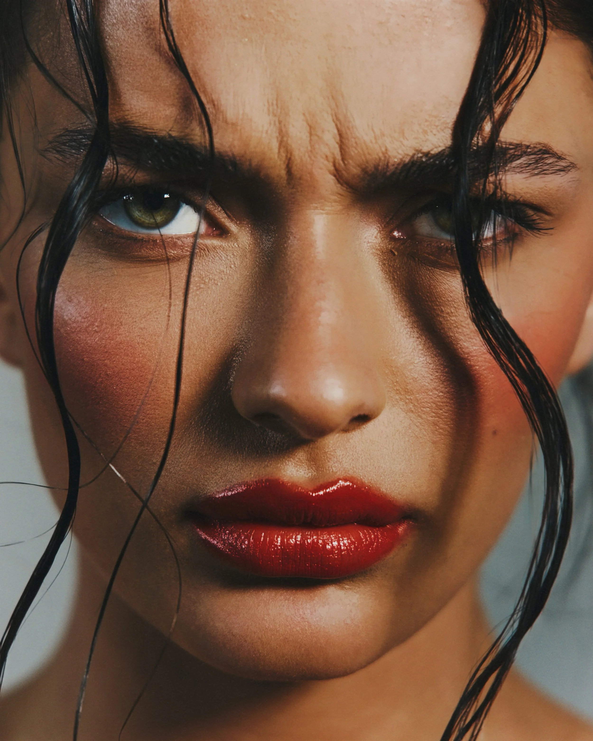 Close-up of a woman's face showing intense green eyes, wet black hair, and shiny red lips.