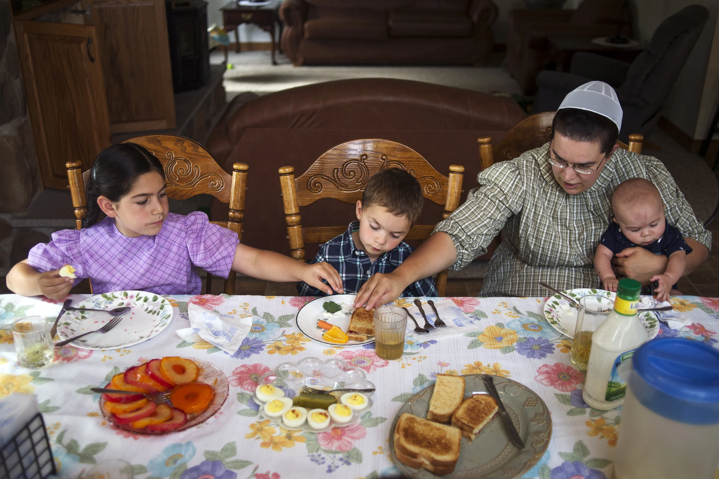 Sophia, 9, left, and Freda, right, check out Adrian's, 4, sandwich to see if there's meat on it as Freda holds onto Theodore, 5 months, during dinner on July 7 in Coleman, Mich.