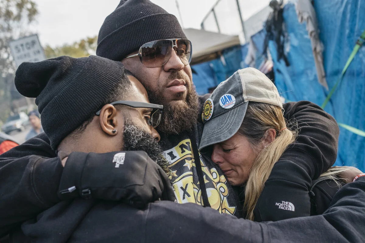  UAW Local 598 alternate committee men Stanley Dulaney, Jr., 34, and Will McIntosh, 38, and member Dawn DeKalita, 48, embrace after hearing that the new UAW GM contract was ratified outside the Flint Assembly Plant in Flint, Mich. on Friday, Oct. 25,