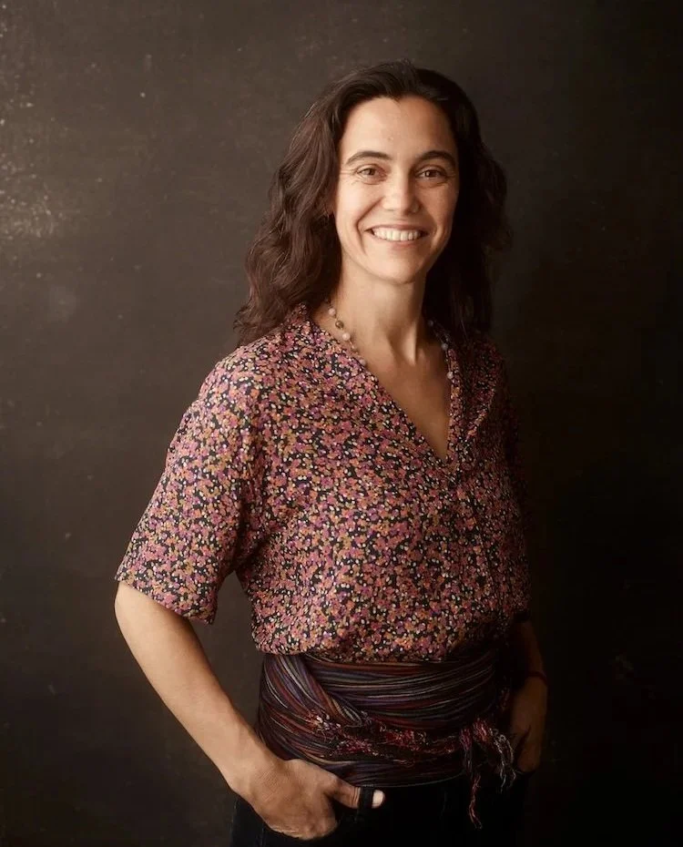 Woman smiling with long hair standing with hands in belt loops in a floral shirt