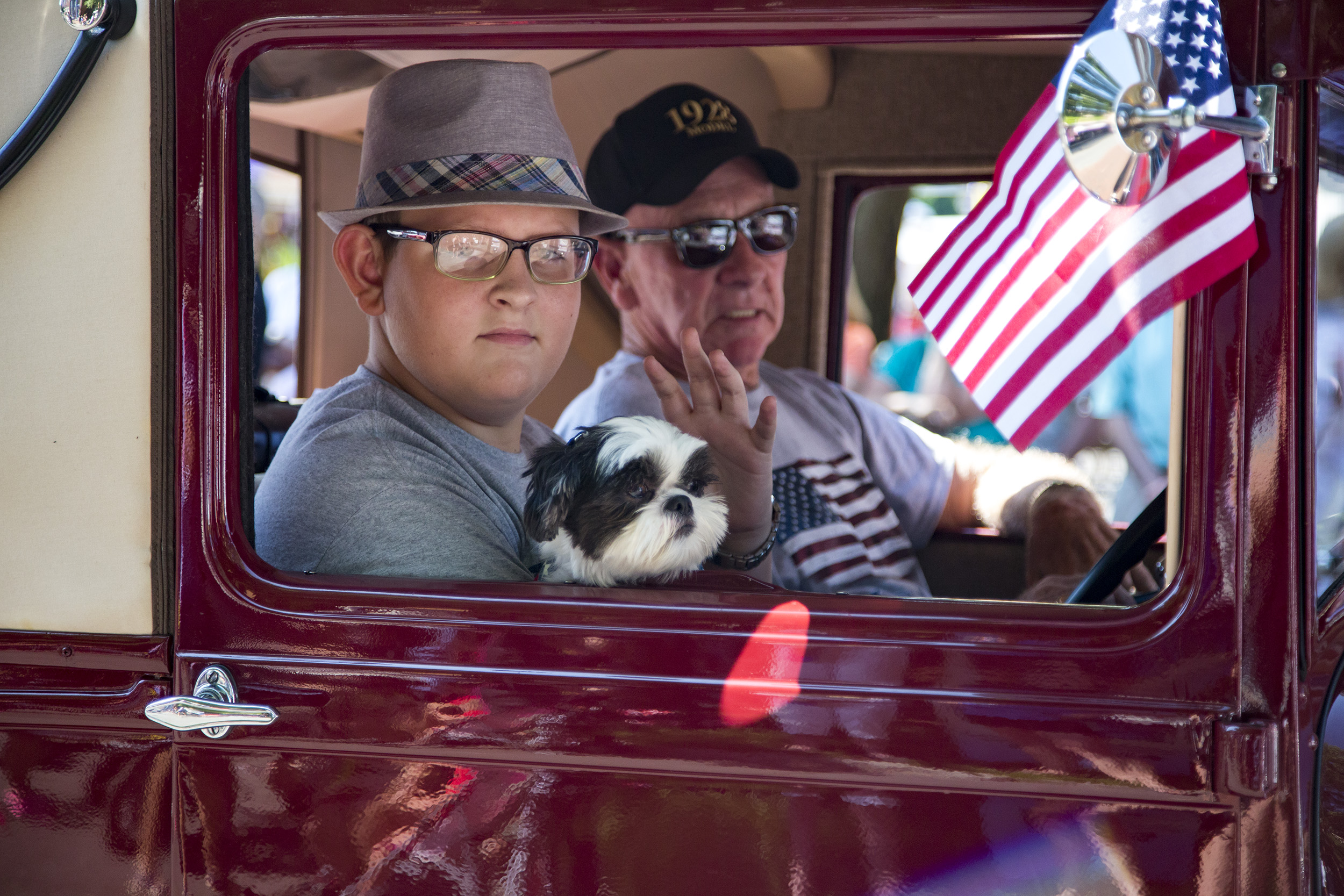 A man, a boy and a dog ride in a shiny antique vehicle, taking us back to another era.
