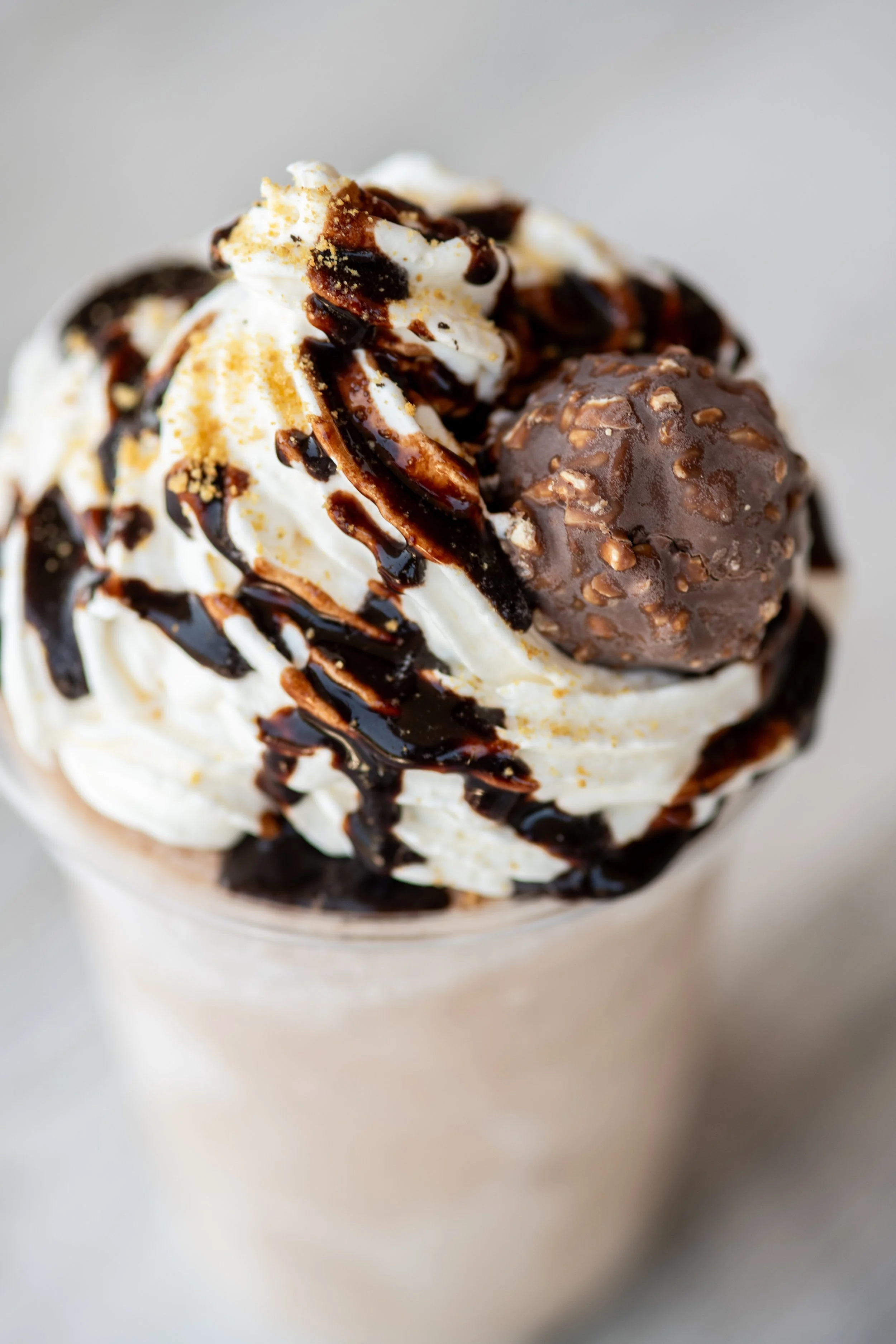Close-up of a chocolate milkshake topped with whipped cream, chocolate syrup, a chocolate truffle, and sprinkled with crushed nuts.