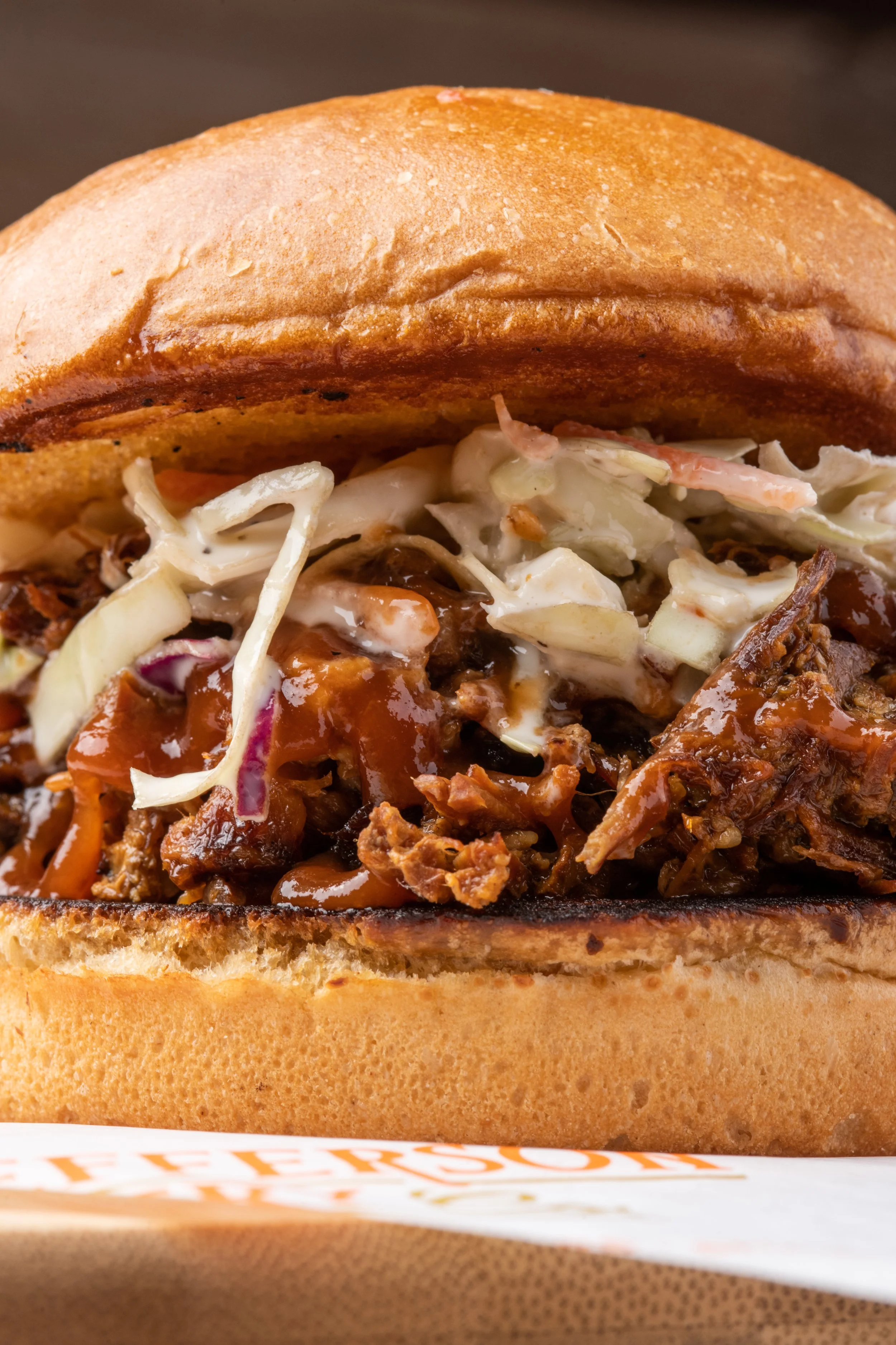 Close-up of a sandwich with shredded meat, coleslaw, and barbecue sauce in a toasted bun.