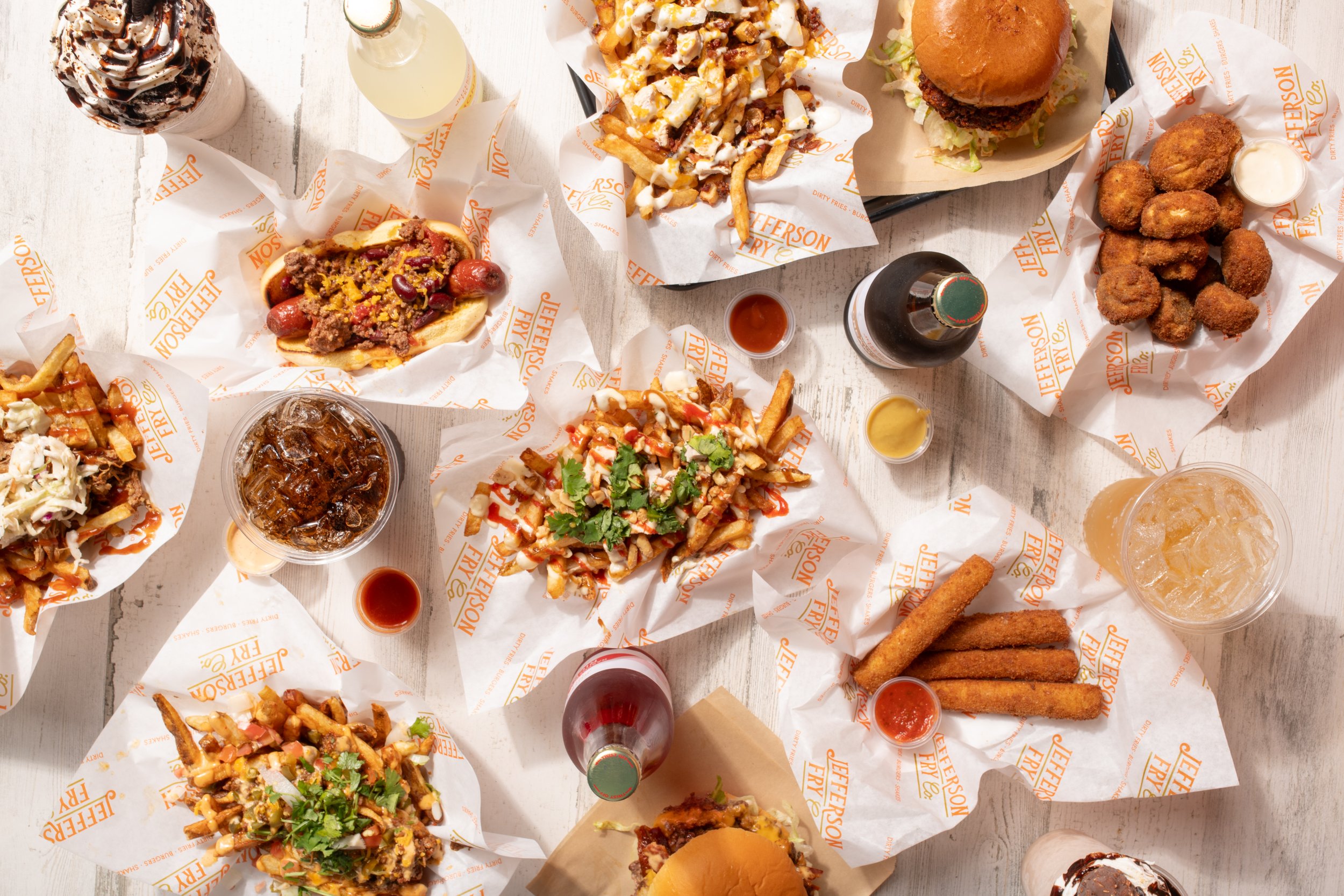 Assorted fast food dishes on a white table, including burgers, fries, fried chicken, nachos, and beverages.