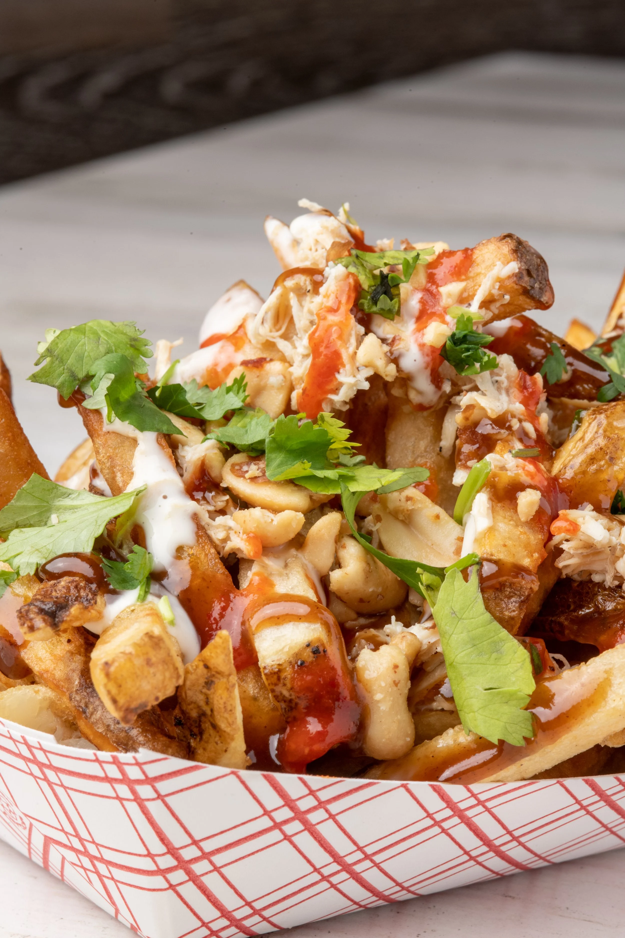 Close-up of a serving of loaded fries topped with chicken, cilantro, and drizzled with hot sauce and ranch dressing.