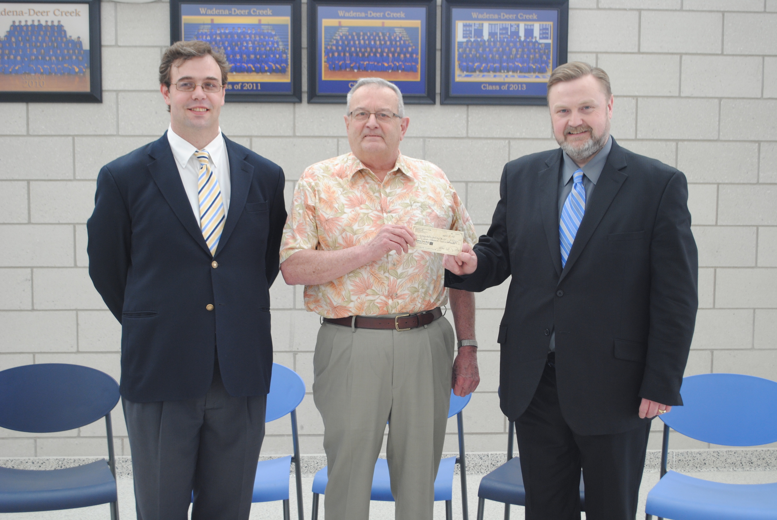 Sam Phillips hands WDC Superintendent Lee Westrum a gift from the estate of Betty Stark on April 9 at WDC Middle/High School. Also pictured is Malcolm Whynott, the attorney who assisted with the distribution of gifts. (Photo by Dana Pavek, WDC Schools)