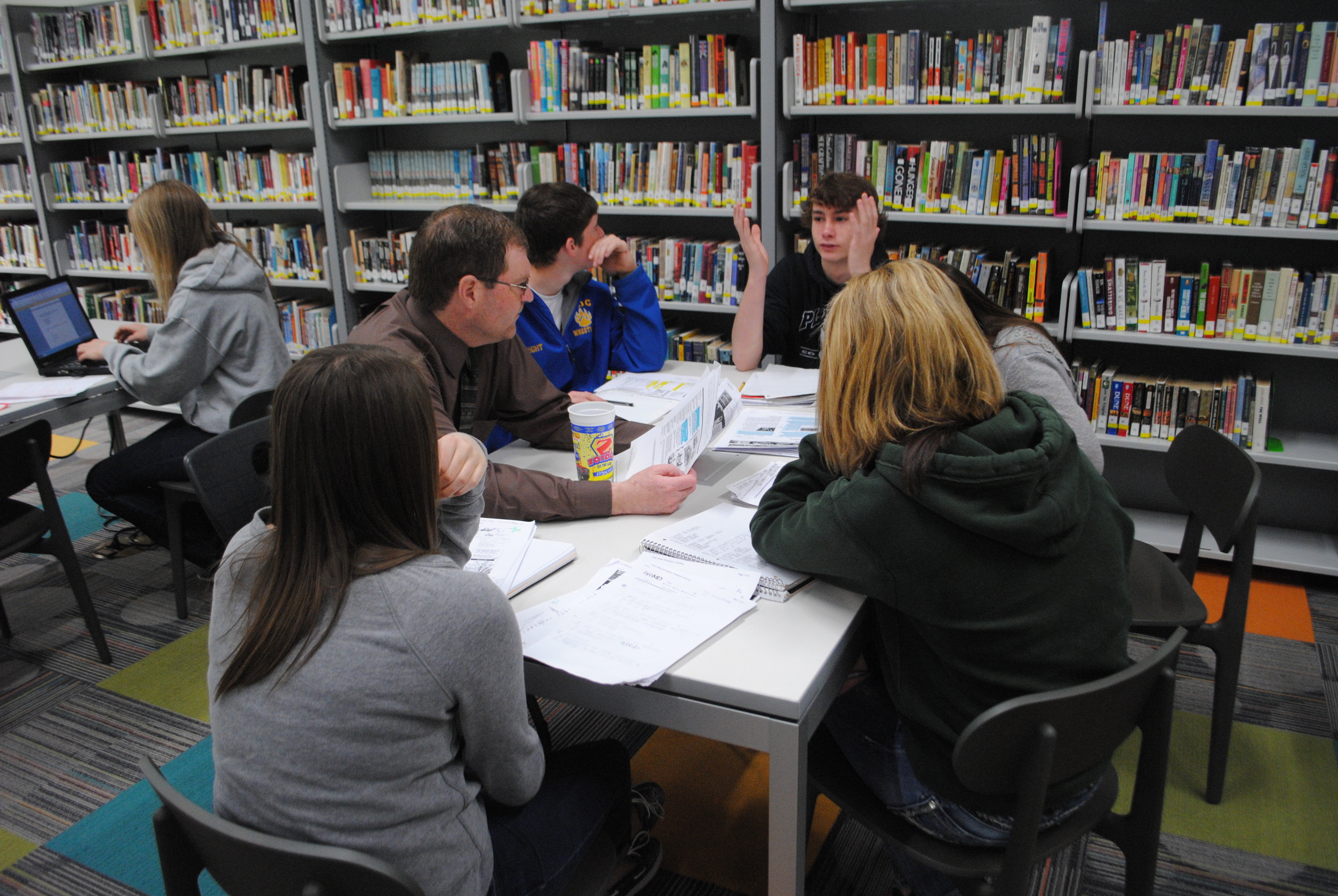 WDC High School Social Studies teacher Robby Grendahl sits with his ninth-grade students as they work on their term papers for Civics. (Photos by Dana Pavek, WDC Schools)