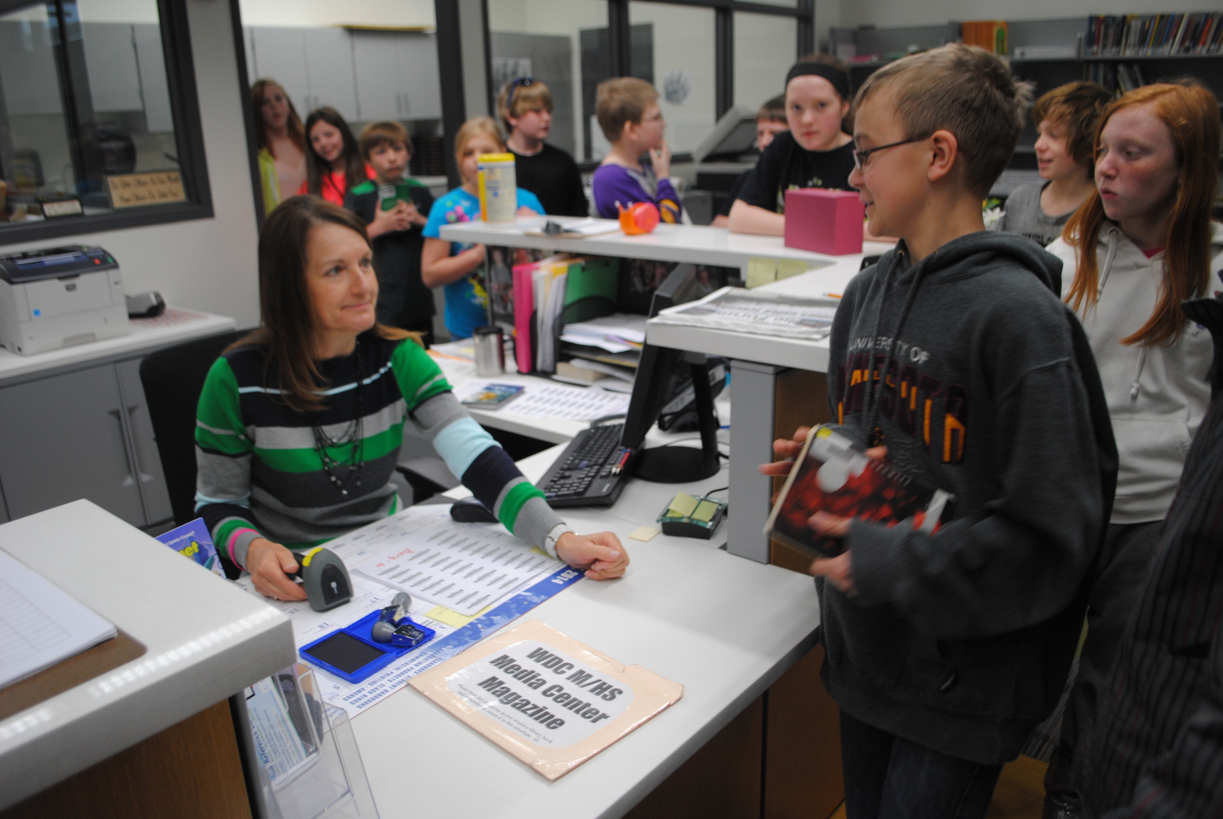 Media Center assistant Kathie Davis takes care of a long line of sixth-grade students from Mrs. Berg's class on Tuesday. Mrs. Davis takes time to chat with students as they return or check out books.