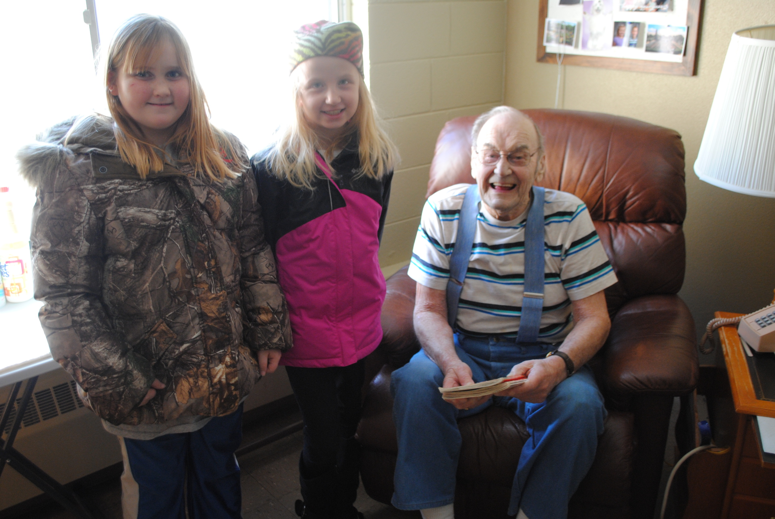 Third-graders Andrea Malone and Hannah Dosdall read Robert Swanson two books during their visit at Fair Oaks Lodge on Wednesday, Feb. 4. After the students finished reading, Swanson dug out a scrapbook and shared stories from his life as a policeman, a farmer and a commercial fisherman with the attentive students. (Photos by Dana Pavek, WDC Schools)