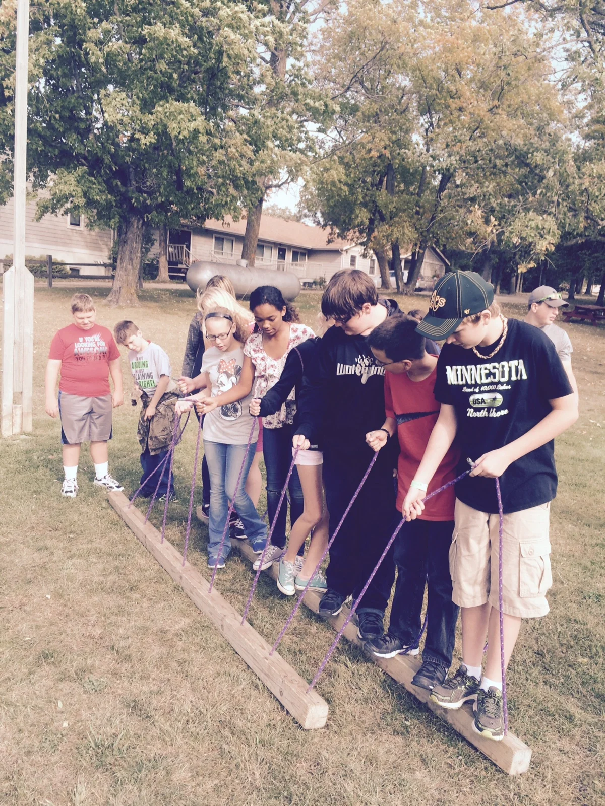 WDC seventh-graders participate in the “Trolley” activity, where each student must have one foot on each side of the trolley. If one person touches the ground or “swamp of poisonous yogurt,” the whole group must start over. The team-building activity was part of a retreat held Sept. 15 at Inspiration Point and Retreat Center near Clitherall. (Photo by Toni Kraska, WDC Schools)