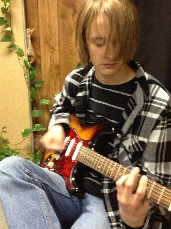    Teen boy plays song on sunburst electric guitar in teacher studio.   