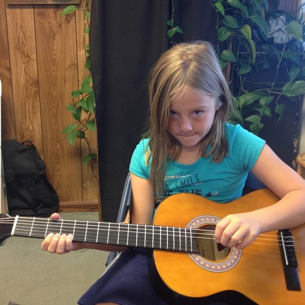   Young girl plays acoustic guitar in left-hand   