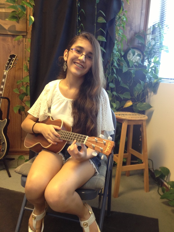    A teen girl with long hair holds ukulele and plays a chord.   