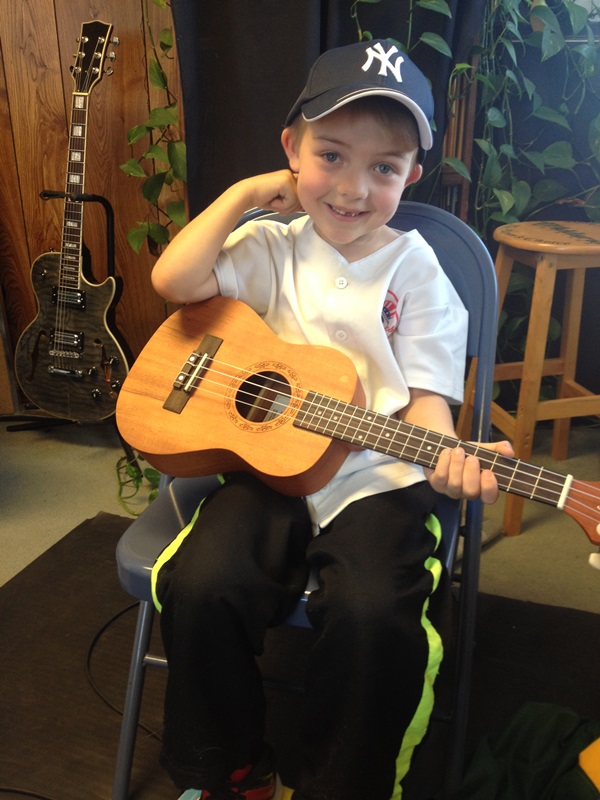    A young boy holds his ukulele and smiles.   