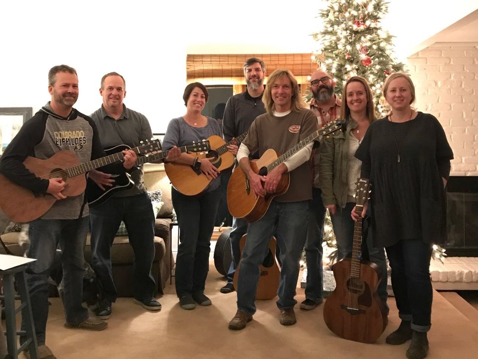    A group of adults and teacher stand together holding instruments following guitar instruction.   