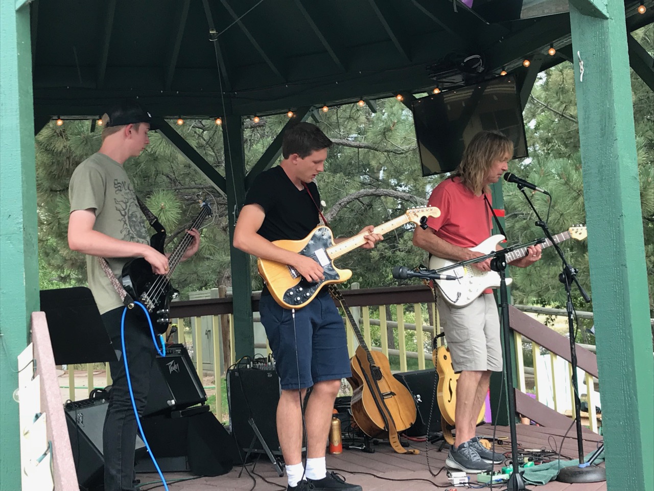    Two teen boys performing on electric guitar with their teacher in band shelter.   