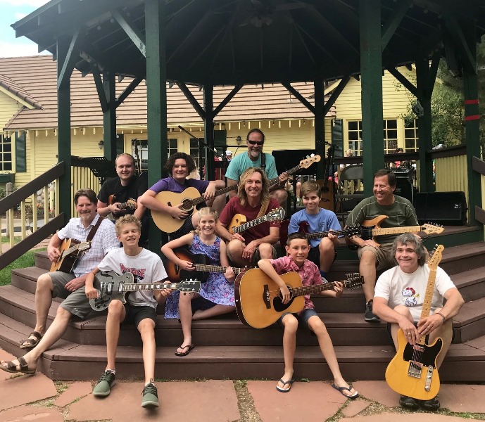    Guitar, bass and ukulele students gather outside with instruments to learn guitar theory.   