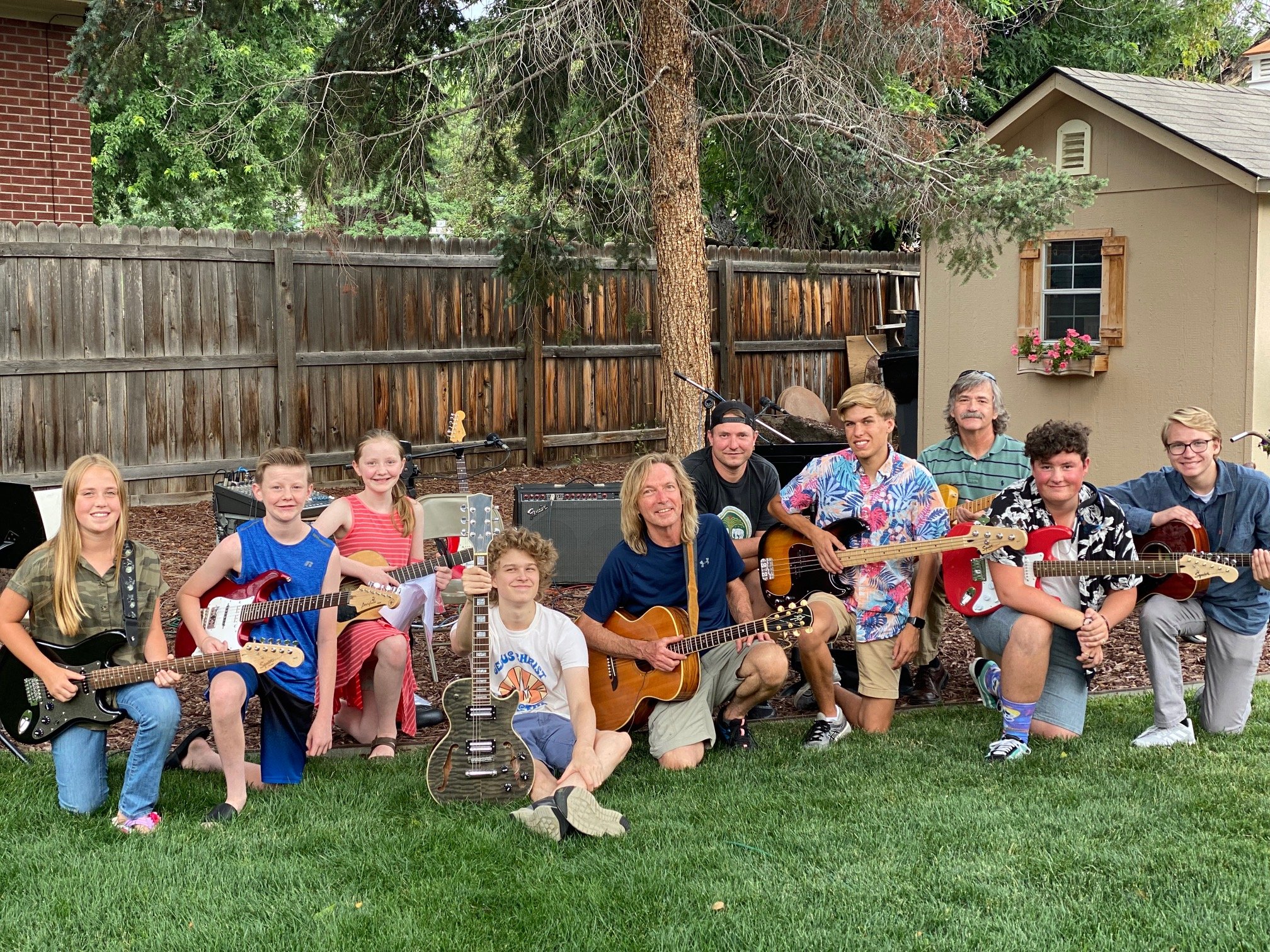    Guitar students gathered in back yard with instruments after performance.   