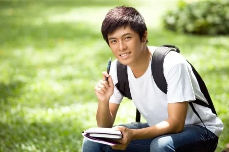 Young man sitting outdoors with a notebook and pen