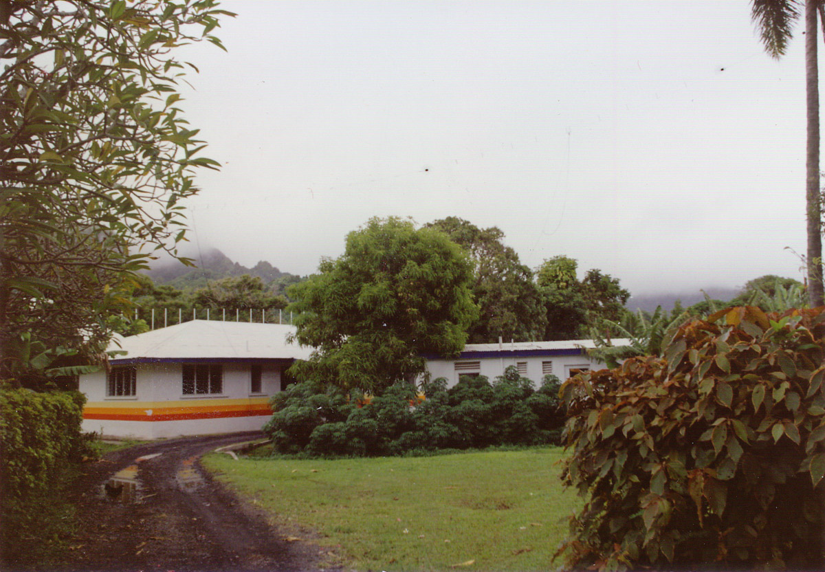 A view from the driveway entrance to the Radio Cook Islands studio in 1993. Insulators on an antenna (T2FD or multiband dipole) can be seen as dark spots against the cloudy sky. A feedline is also seen rising above the left side of the building. (Photo: Guy Atkins)