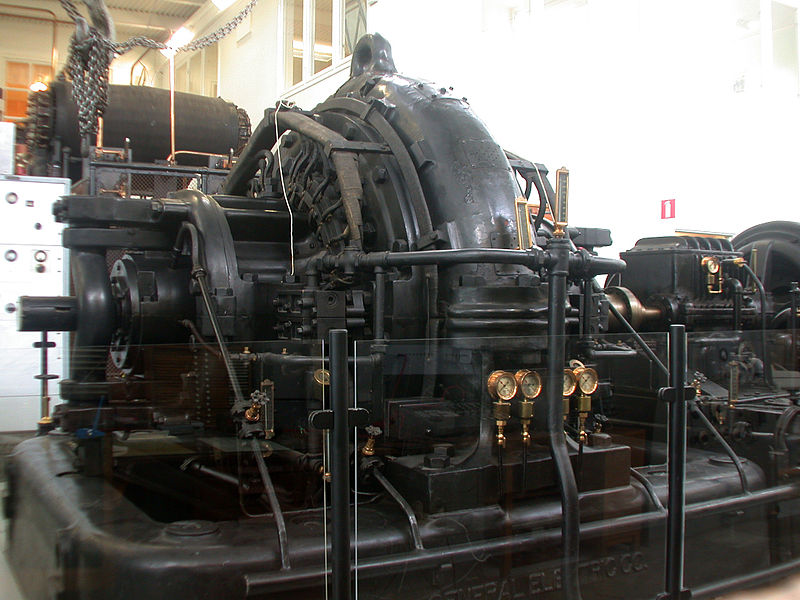 ALEXANDERSON ALTERNATOR IN THE GRIMETON VLF TRANSMITTER. THE DRIVE MOTOR IS AT THE EXTREME RIGHT; THE SPEED-INCREASER GEARBOX IS JUST TO ITS LEFT. NOTE THE BRONZE-COLORED SHAFT COUPLING. IMAGE AND CAPTION COURTESY GUNTHER TSCHUCH AND WIKIMEDIA COMMONS.
