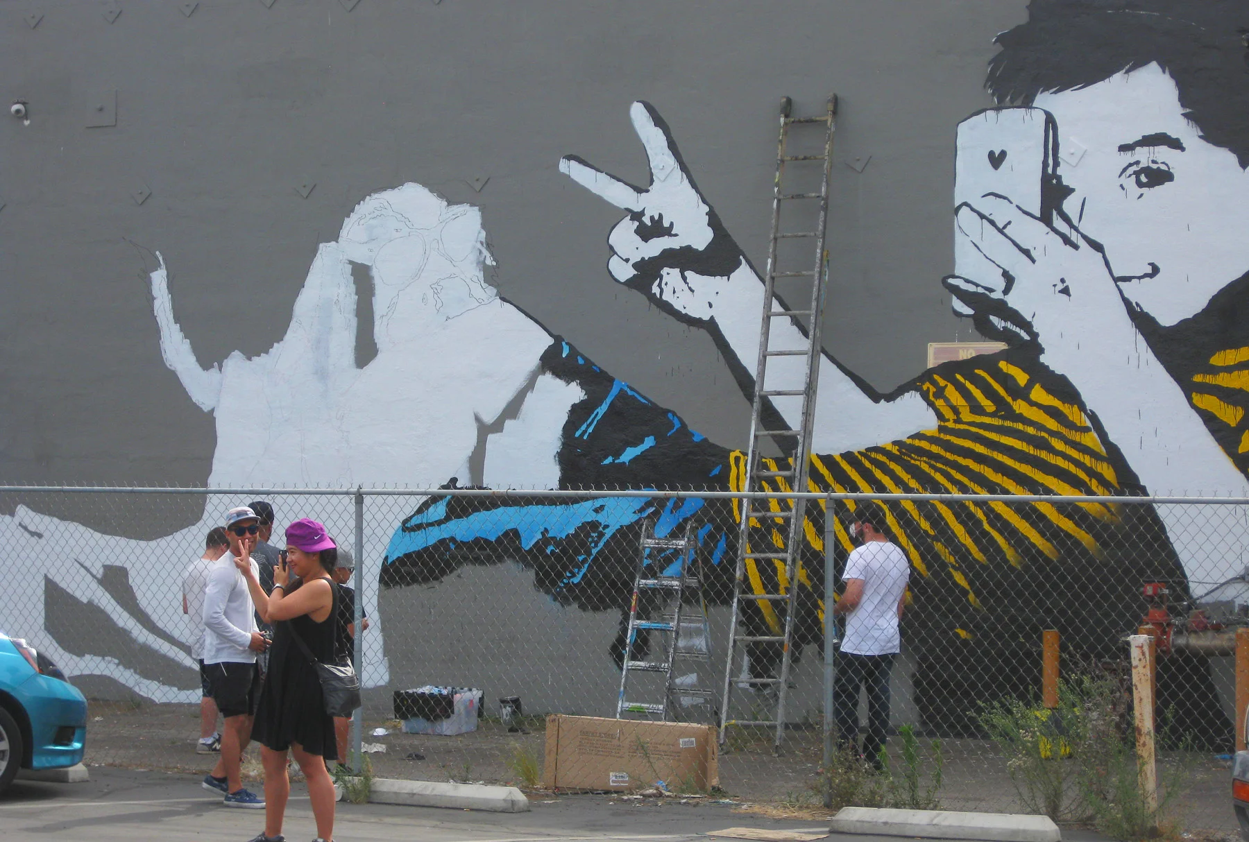 A visitor poses in front of the BumbleBee street art team painting a mural for Pow Wow Long Beach at Berlin Bistro in the East Village.