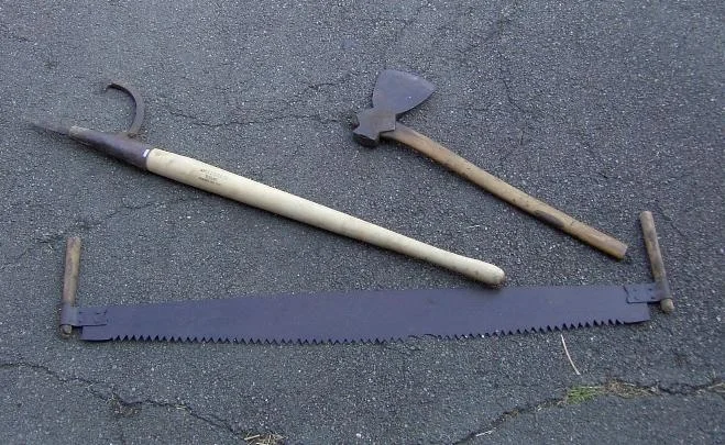 From right to left, an axe, a peeve, and a two man cross cut saw.
