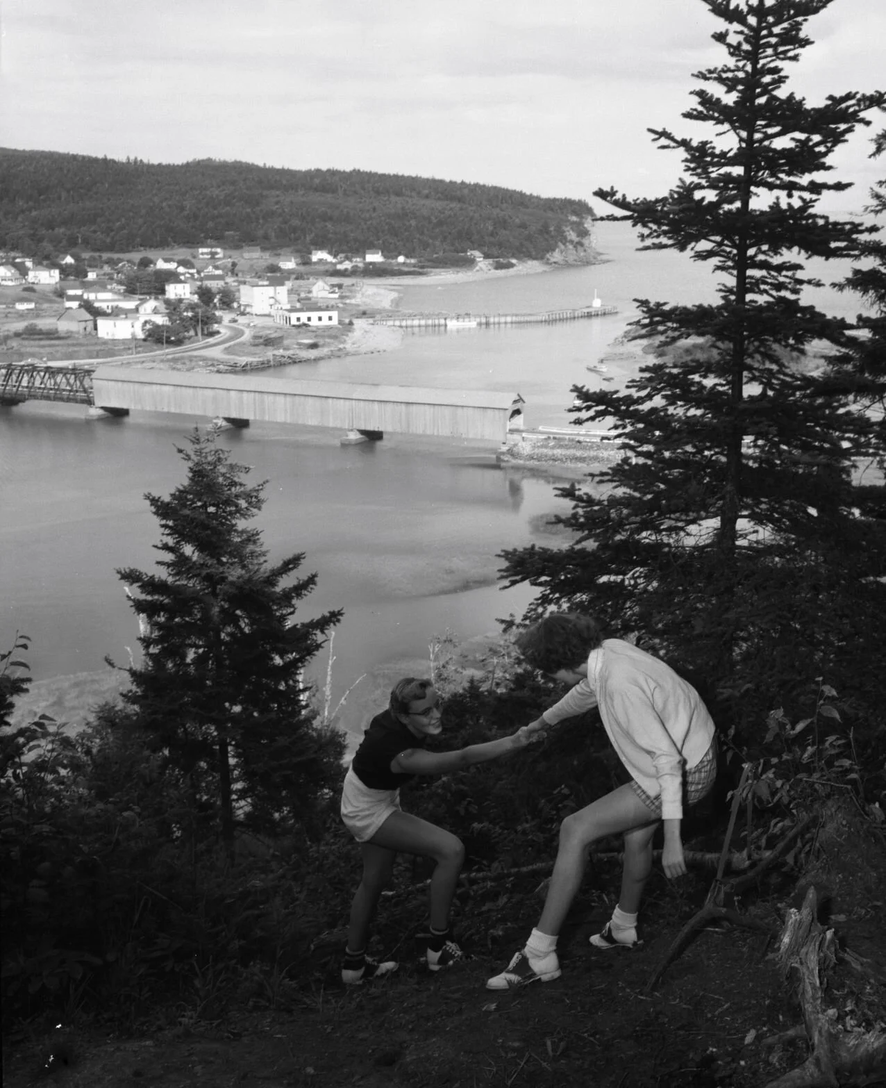 Pair climbing up a hillside near Alma. The covered bridge and the town can be seen in the background, c.1950. Photo from Archives New Brunswick -P93-AL-228.jpg