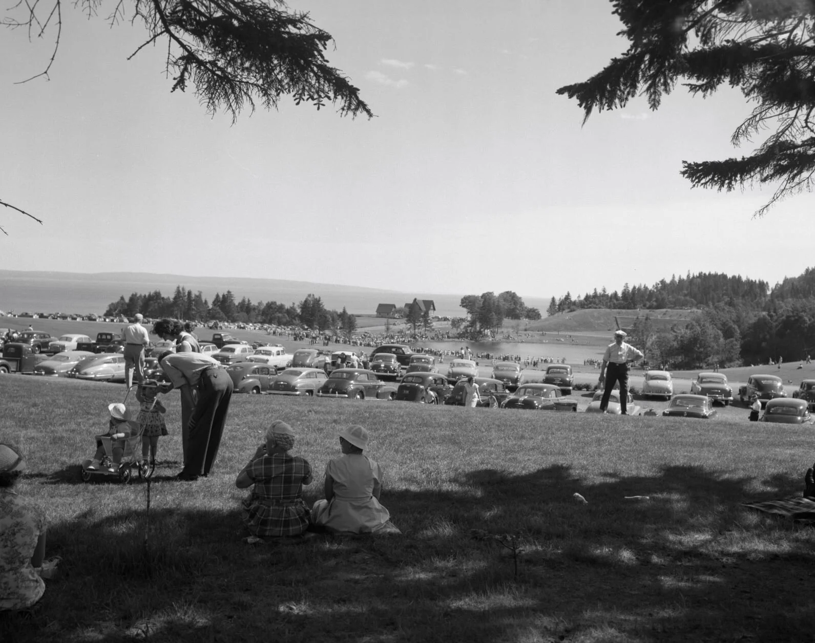 Large group of people and parked cars around lake near headquarters area, Fundy National Park. From Archives New Brunswick P93-AL273..