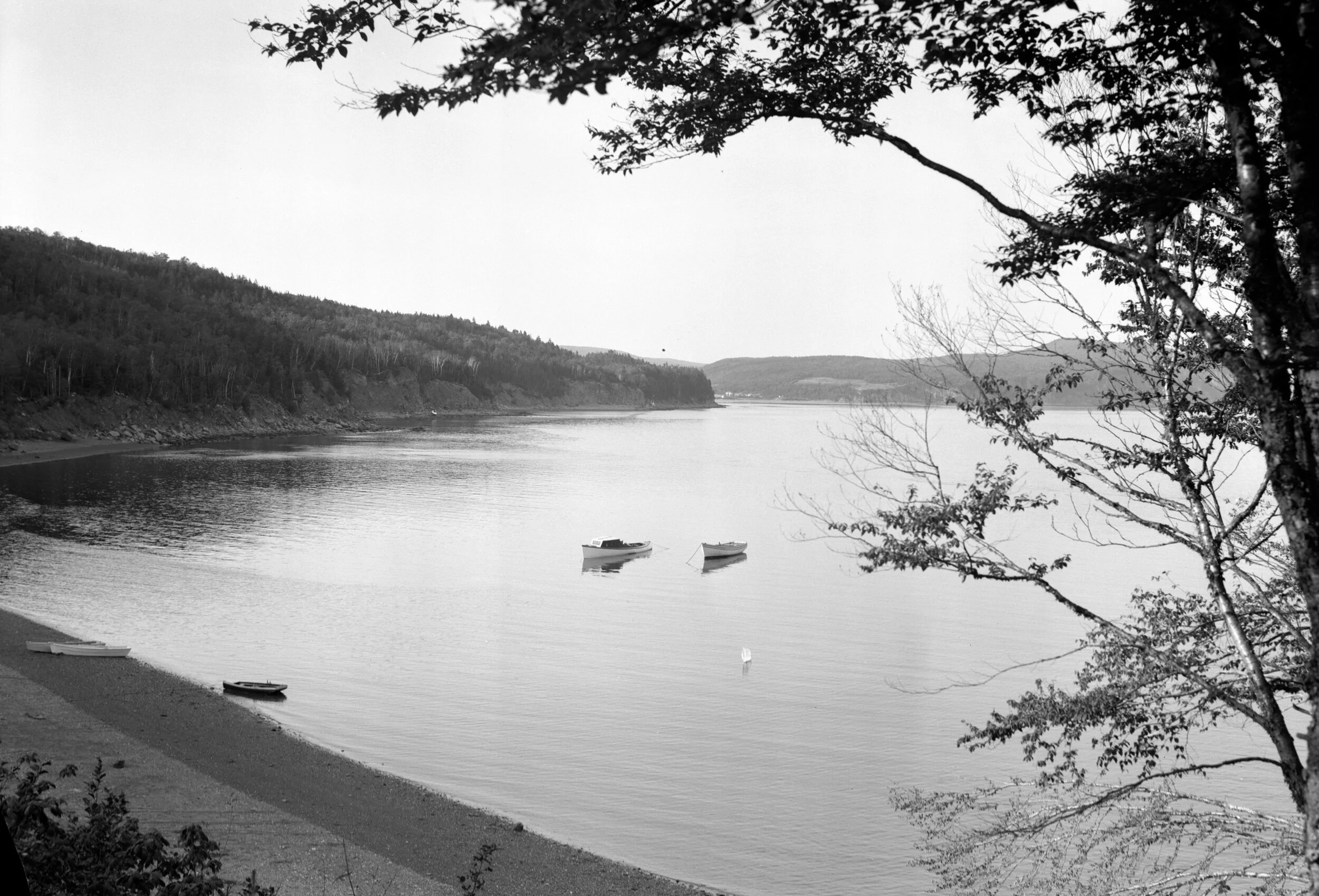 Shoreline of cove with three small boats on shore and two anchored in cove, vicinity of Herron Cove, 1940. From Archives New Brunswick P93-AL-26