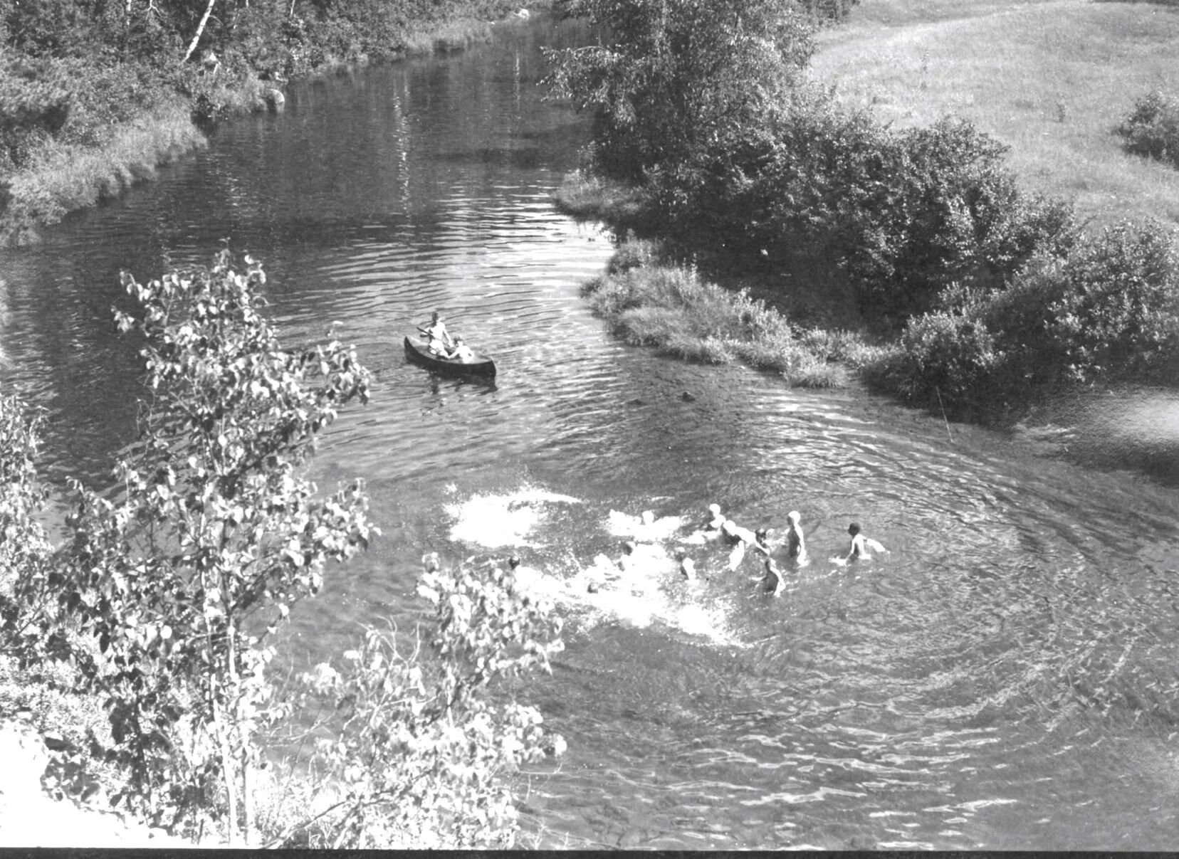 Group of young people swimming in river also two sitting in a canoe on the river, Camp Hermit Thrush near Elgin, c.1940.. From Archives New Brunswick. P93-AL-39