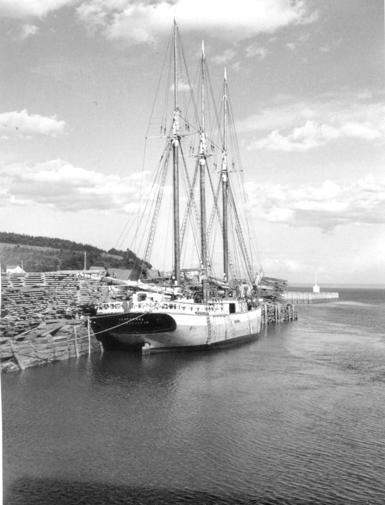 Large sail ship, name on ship [Peaceland] sitting along side dock which is piled with lumber . From Archives New Brunswick.