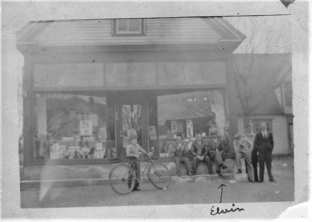 A group of boys one Sunday afternoon in front of Anderson’s Store. This is owned by Winona’s father. The boy on the left looking at the little boy with the bicycle is one of my brothers. the arrow points to Elvin. From the Albert County Museum Colle…