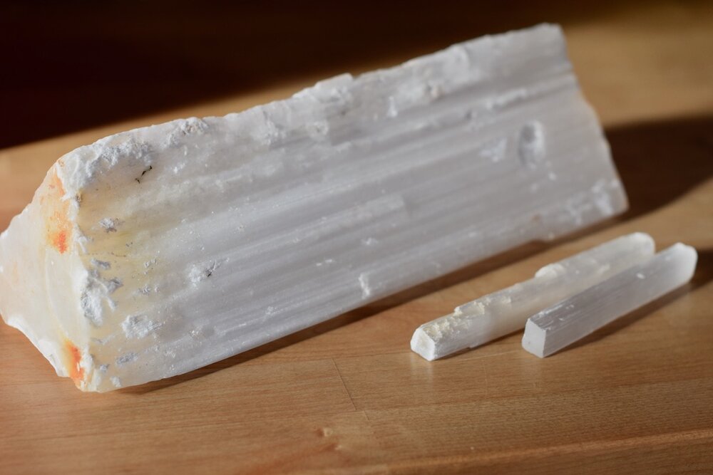Photo of three selenite rods with raw iron parent material on the largest rod, on oak counter top in golden light