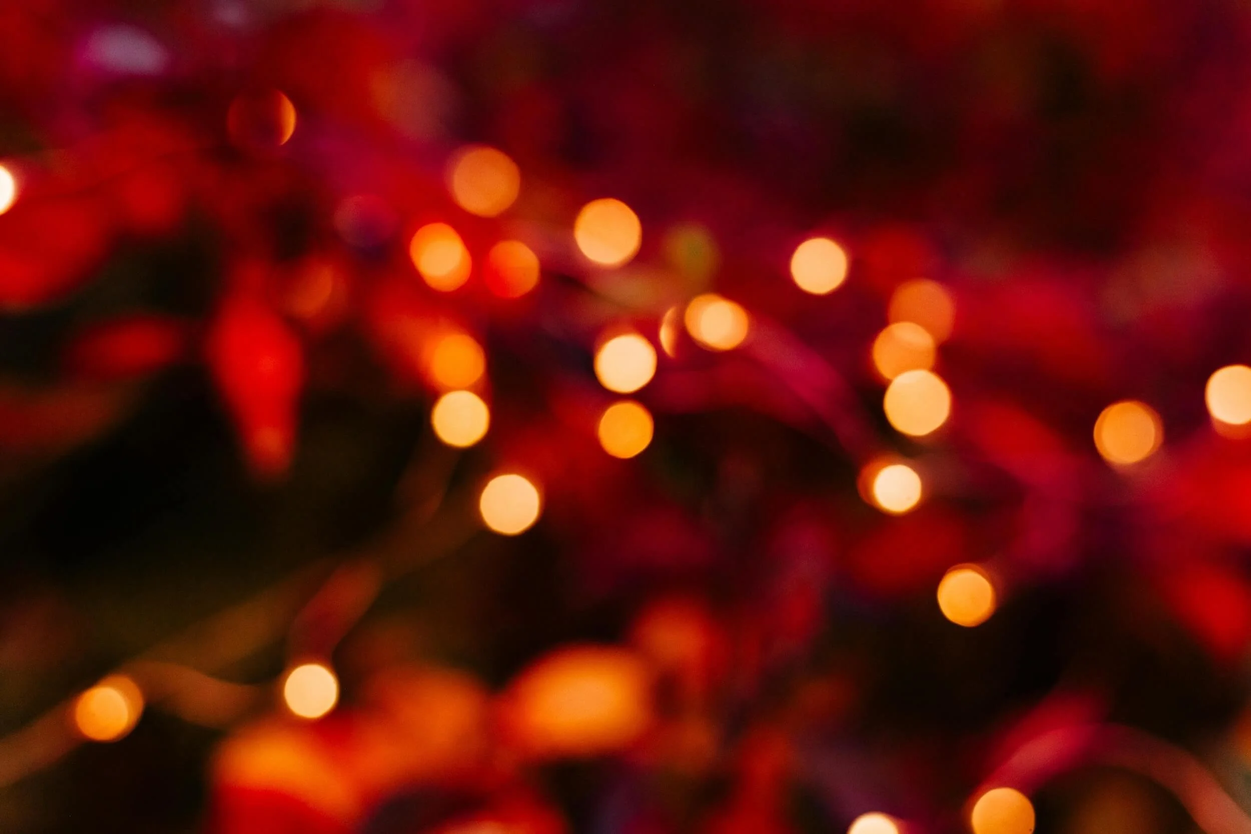 Blurred image of colorful Christmas lights, predominantly red and orange.