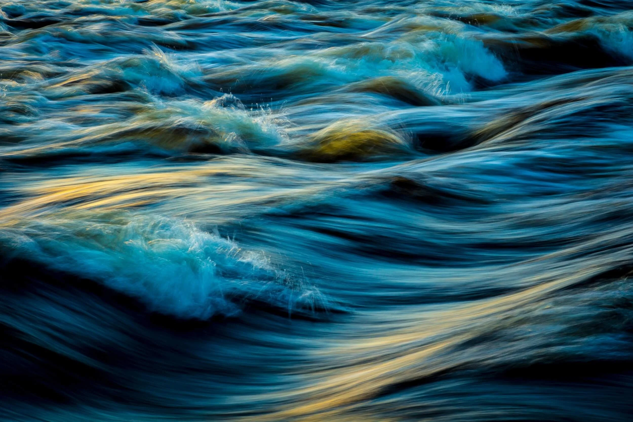 Close-up of moving water with waves and ripples in shades of blue, black, and hints of white.
