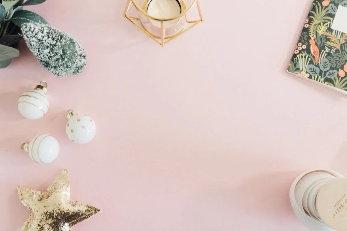Photo of pink surface with gold and white ornaments, a jungle style journal, and candle holders by Uby Yanes on Unsplash