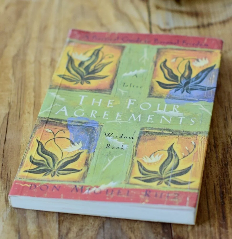 Photo of book, The Four Agreements on wooden table, by Amanda Linette Meder