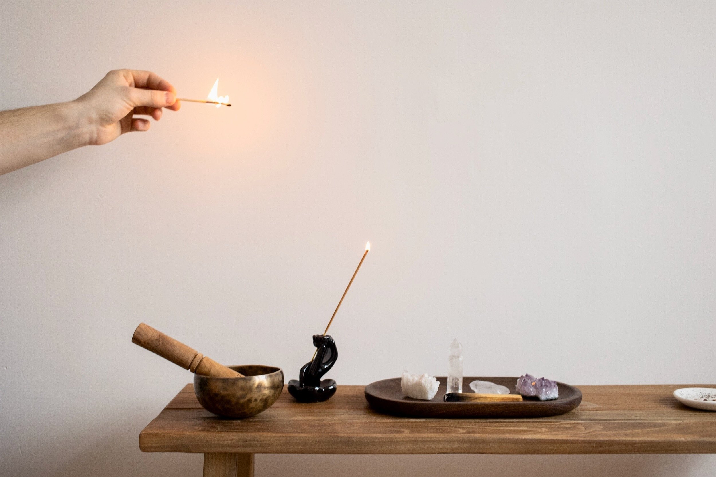 Photo of person lighting an incense on tables with singing bowl and crystals by EKATERINA  BOLOVTSOVA on Pexels