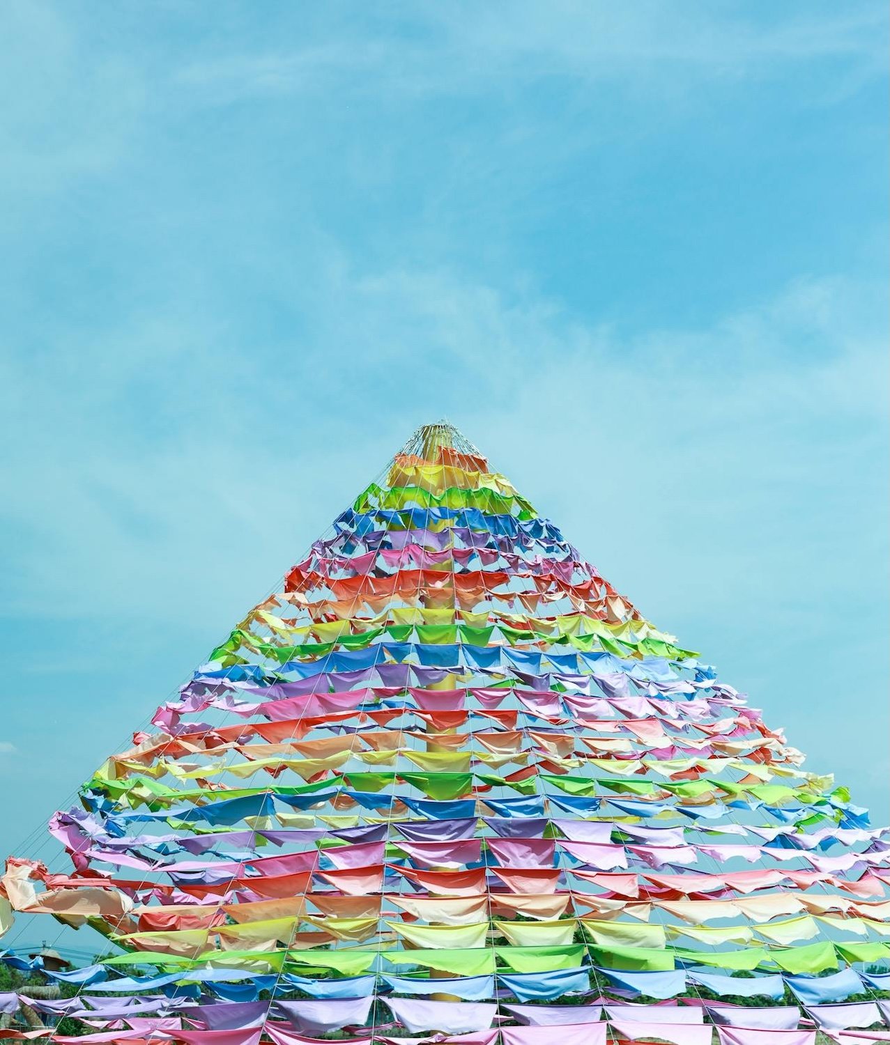 Colorful layered fabric or paper decorations arranged in a pyramid shape against a blue sky.